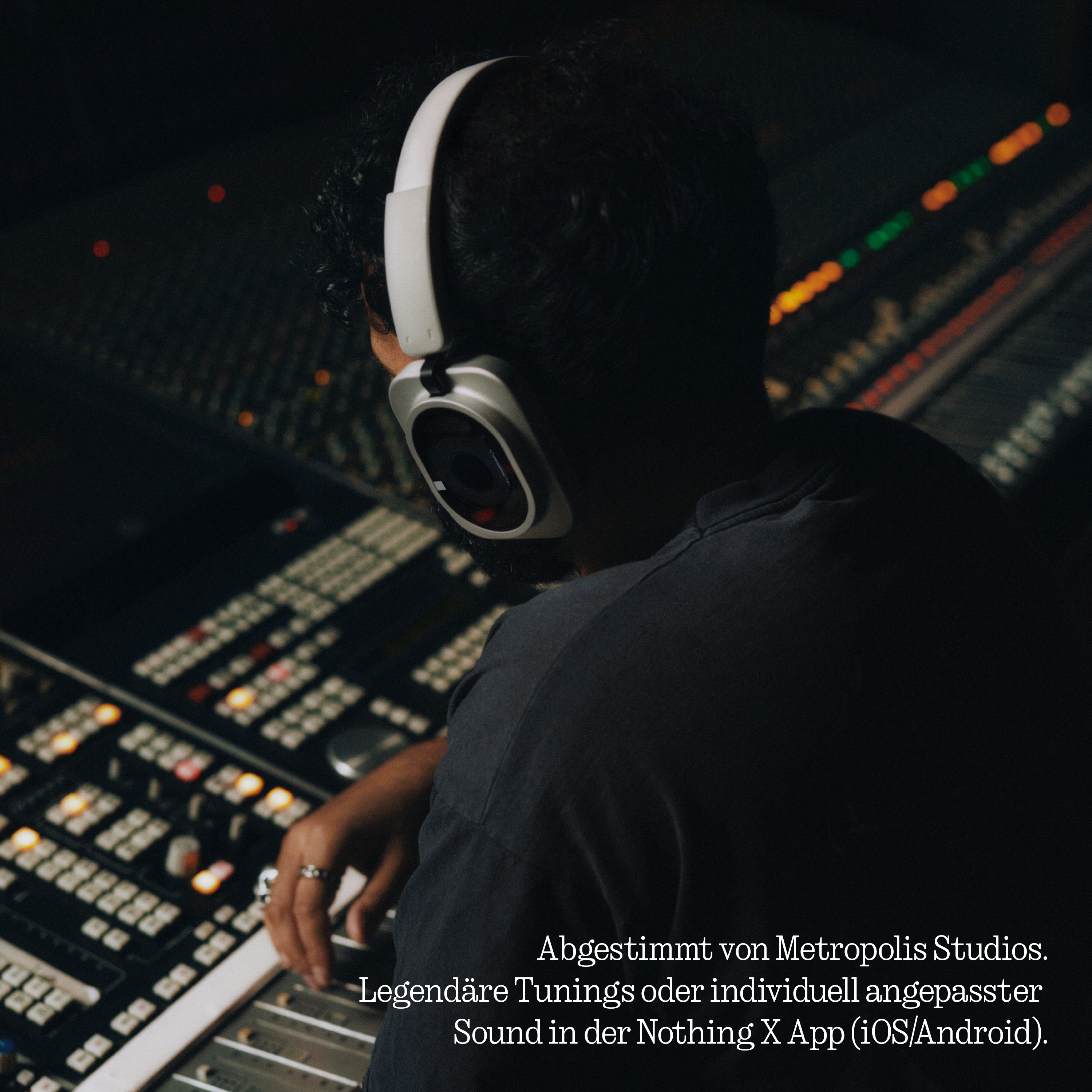 Tontechniker mit weißem Kopfhörer vor großem Mischpult in abgedunkeltem Studio.