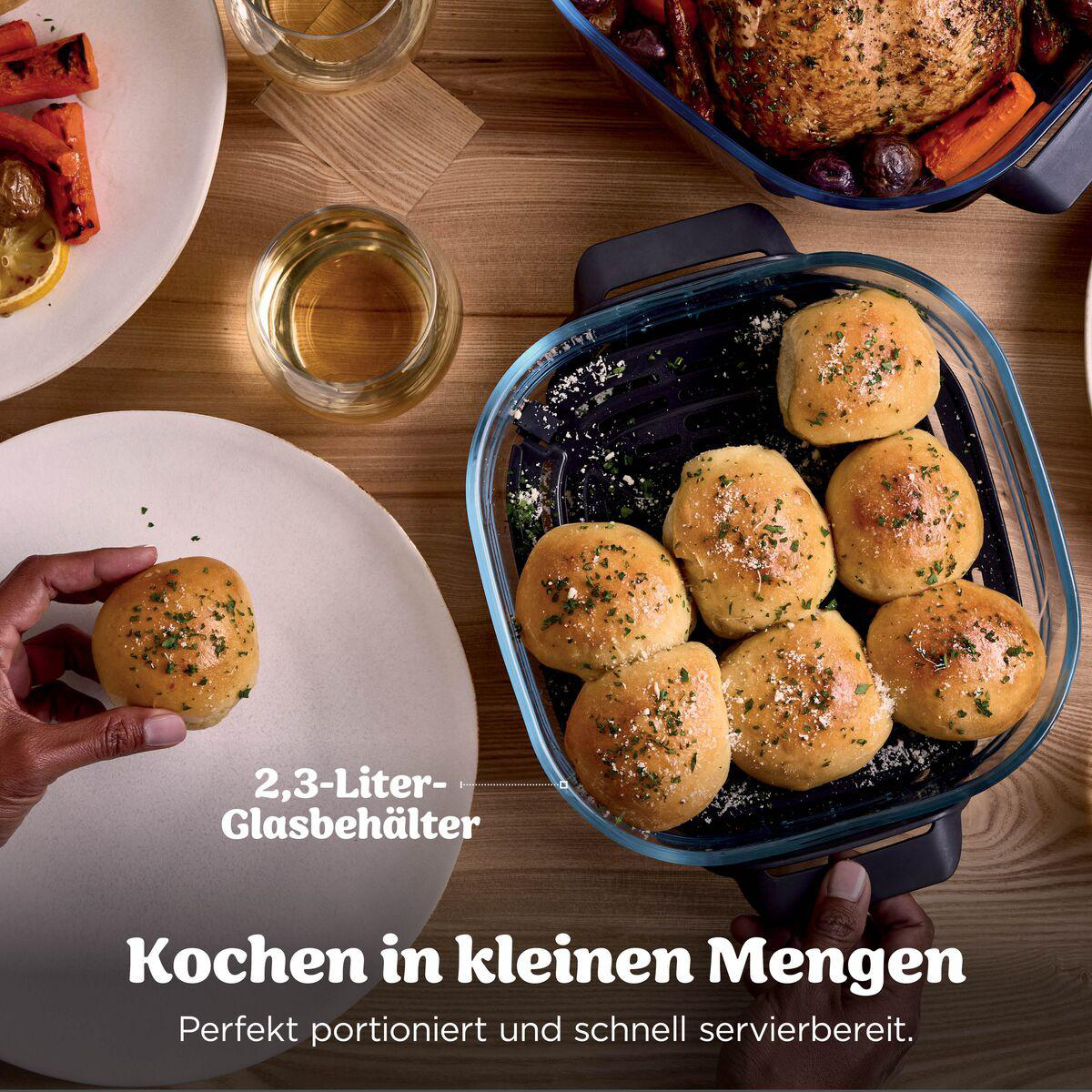 Frisch gebackene Brötchen in einer blauen Glasauflaufform, umgeben von Tellern mit Essen auf Holz.