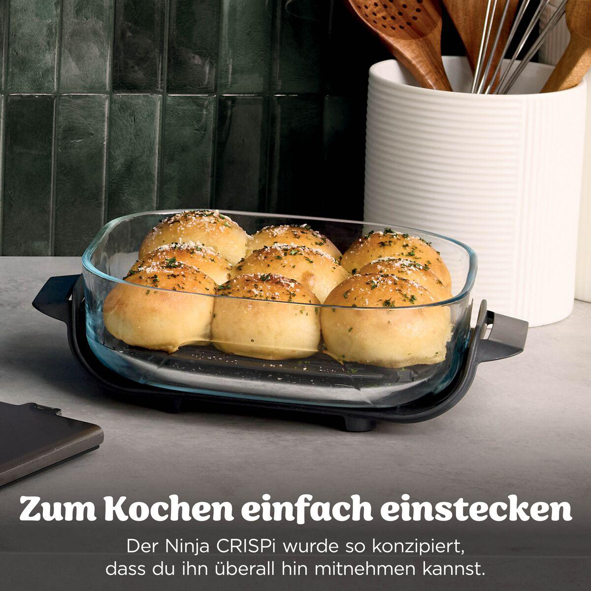 Glasform mit gebackenen Brötchen auf dunkler Basis in moderner Küche.