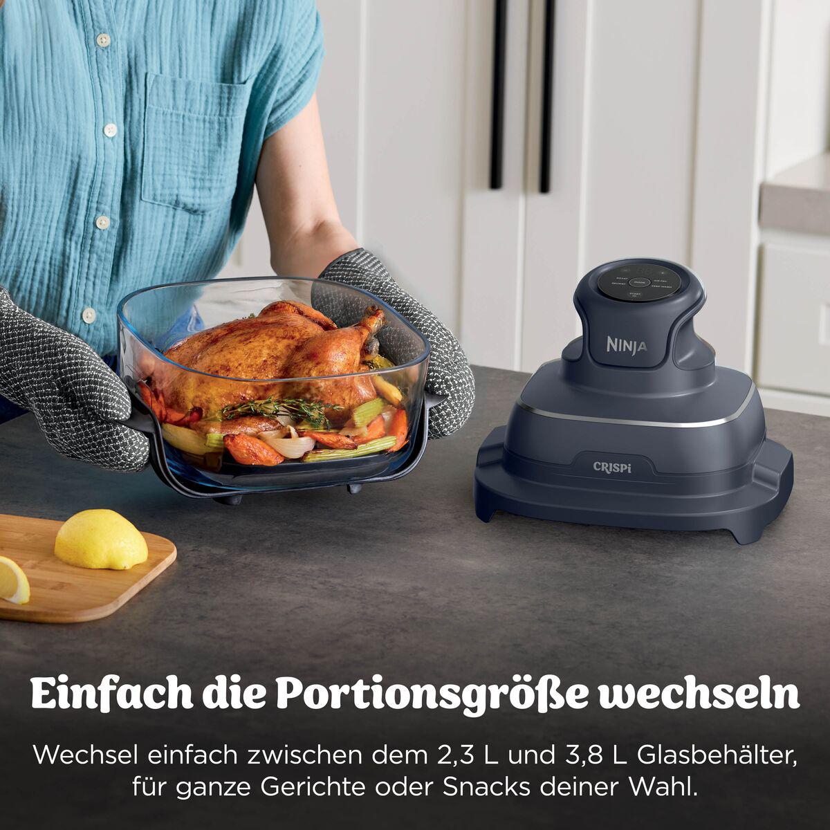 Person in Ofenhandschuhen hält eine Glasform mit ganzem Hähnchen und Gemüse vor einer grauen Ninja Crispi.
