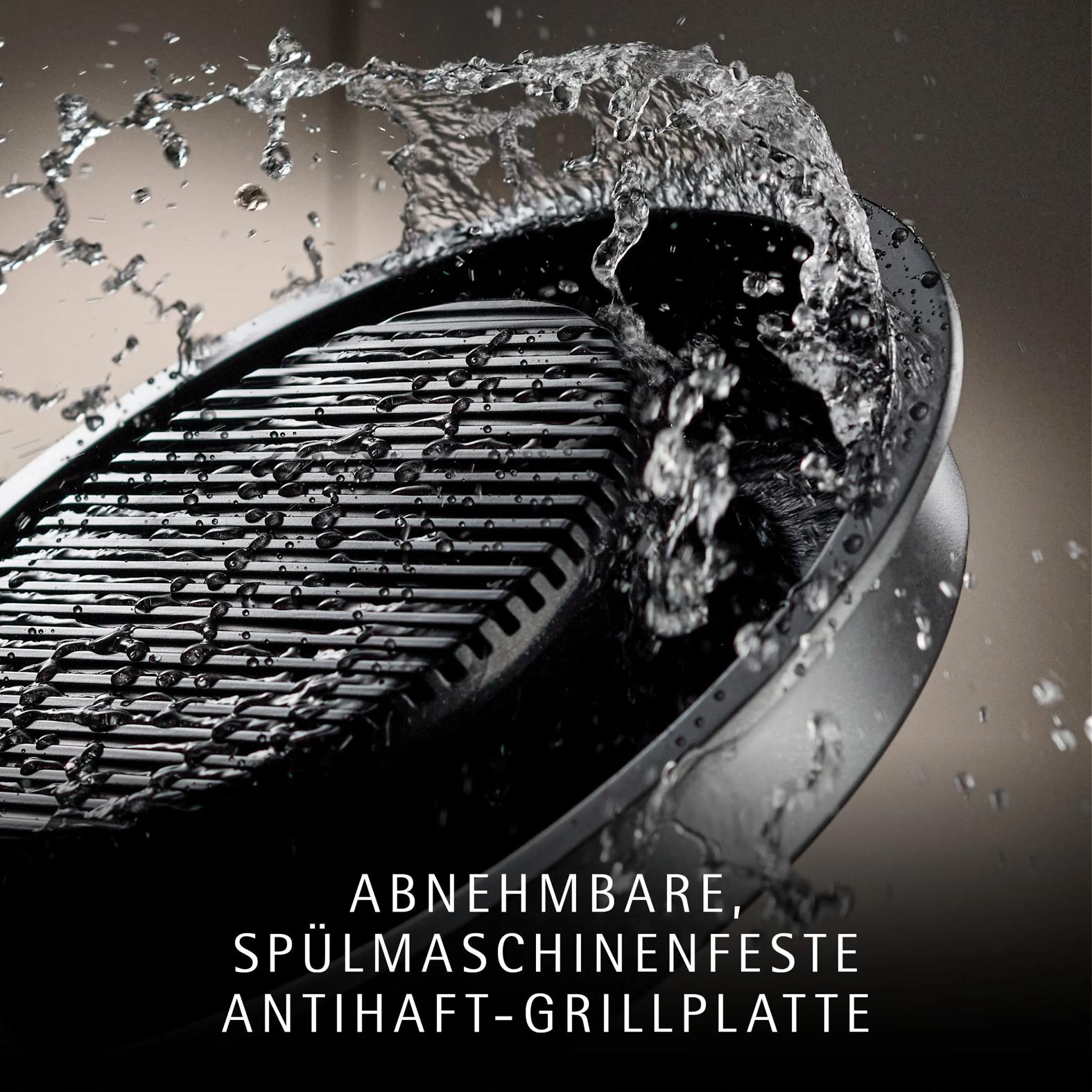 Wasserspritzer treffen auf eine schwarze Grillplatte mit dem Text: Abnehmbare, spülmaschinenfeste Antihaft-Grillplatte.