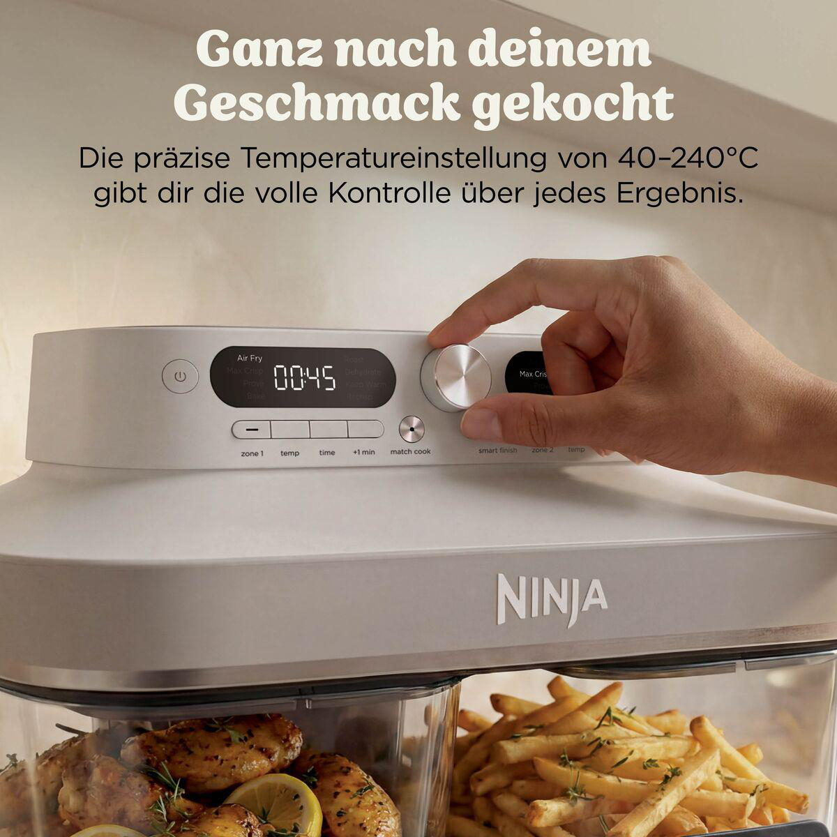 Hand bedient den silbernen Drehregler einer weißen Ninja Heißluftfritteuse, mit Lebensmitteln in den Schubladen.