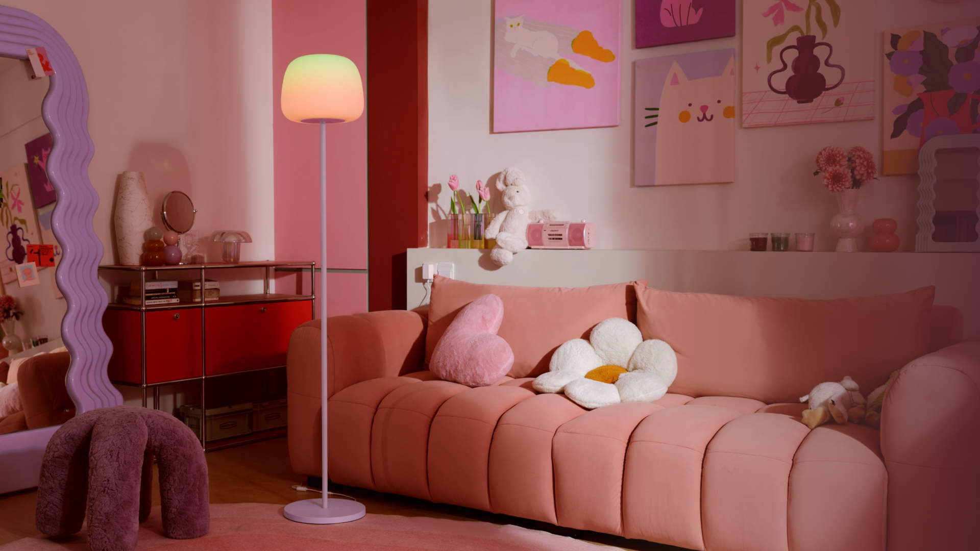 Ein rosafarbenes Wohnzimmer mit einem bequemen Sofa, pastellfarbenen Kissen, einer Stehlampe und Kunstdrucken an der Wand.