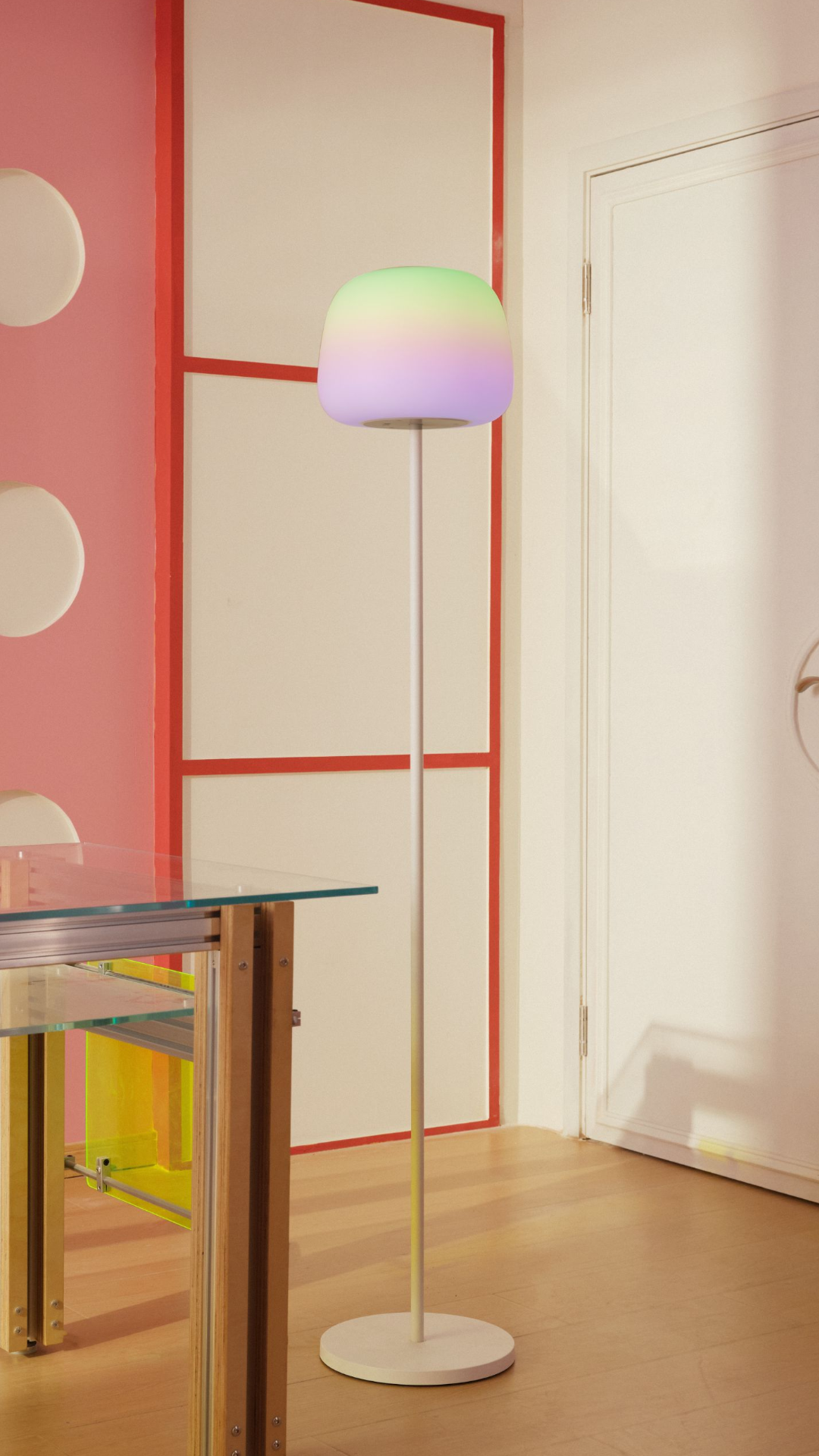 Eine Stehlampe mit grün-violettem Schirm steht in einem farbigen Zimmer.
