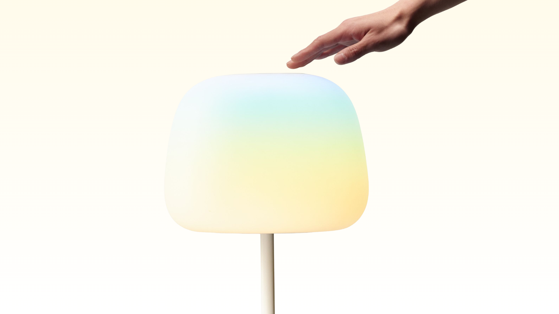 Eine Hand berührt eine kuppelförmige, leuchtende Lampe auf einem dünnen Ständer vor weißem Hintergrund.