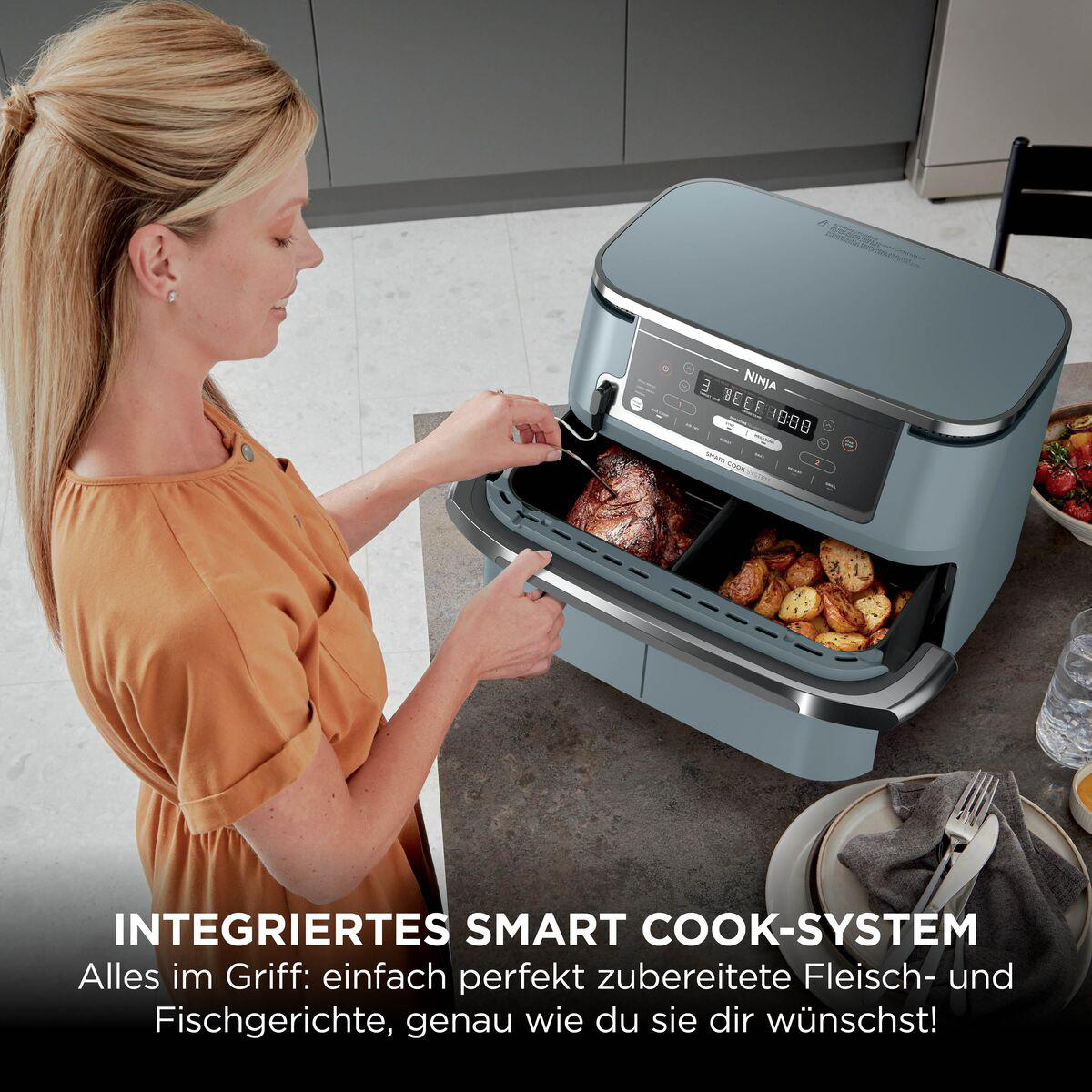 Eine blonde Frau überprüft mit einem Fleischthermometer Fleisch und Kartoffeln in einer Heißluftfritteuse.