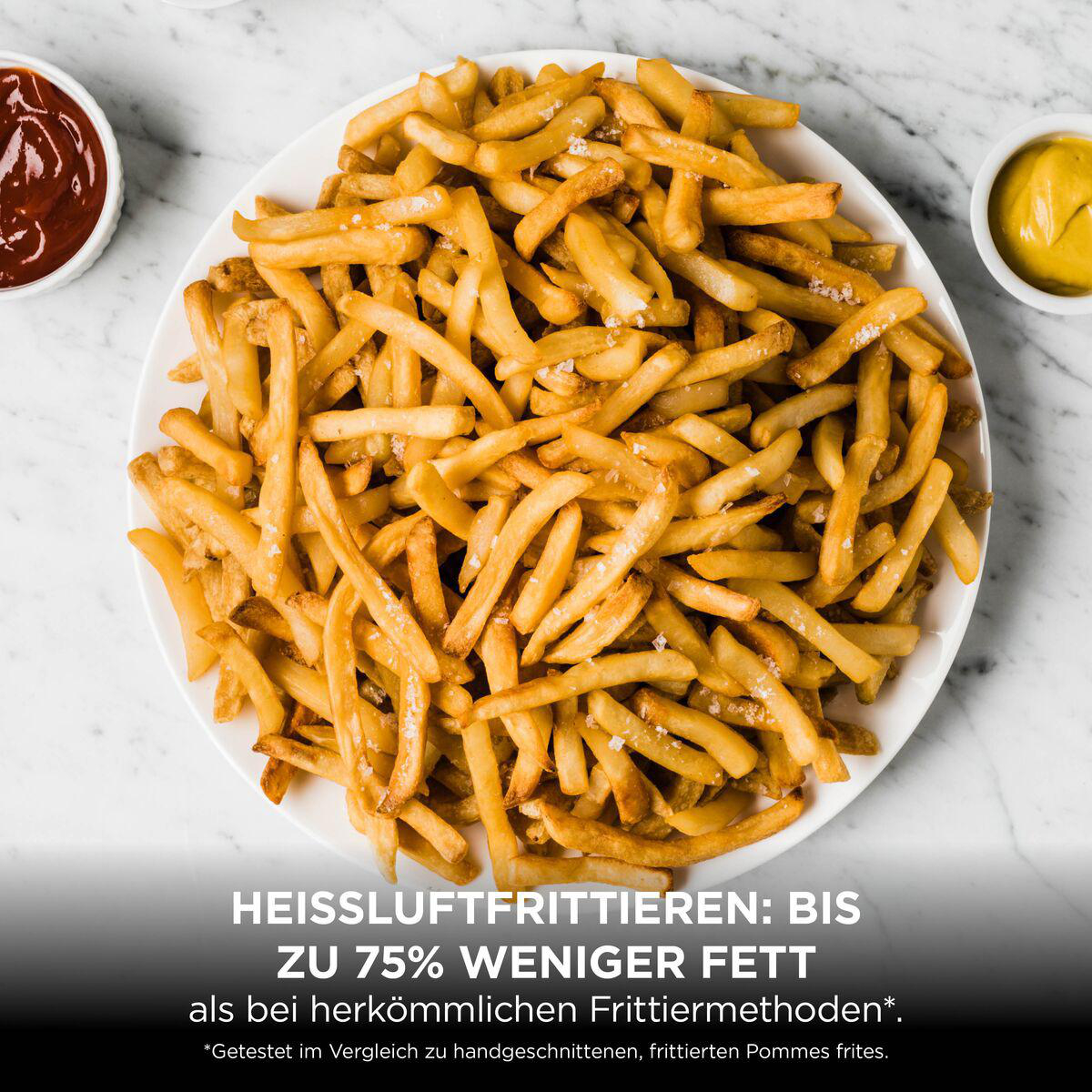 Eine weiße Schüssel mit goldenen Pommes frites, dazu Ketchup und Senf auf einem marmorierten Tisch.