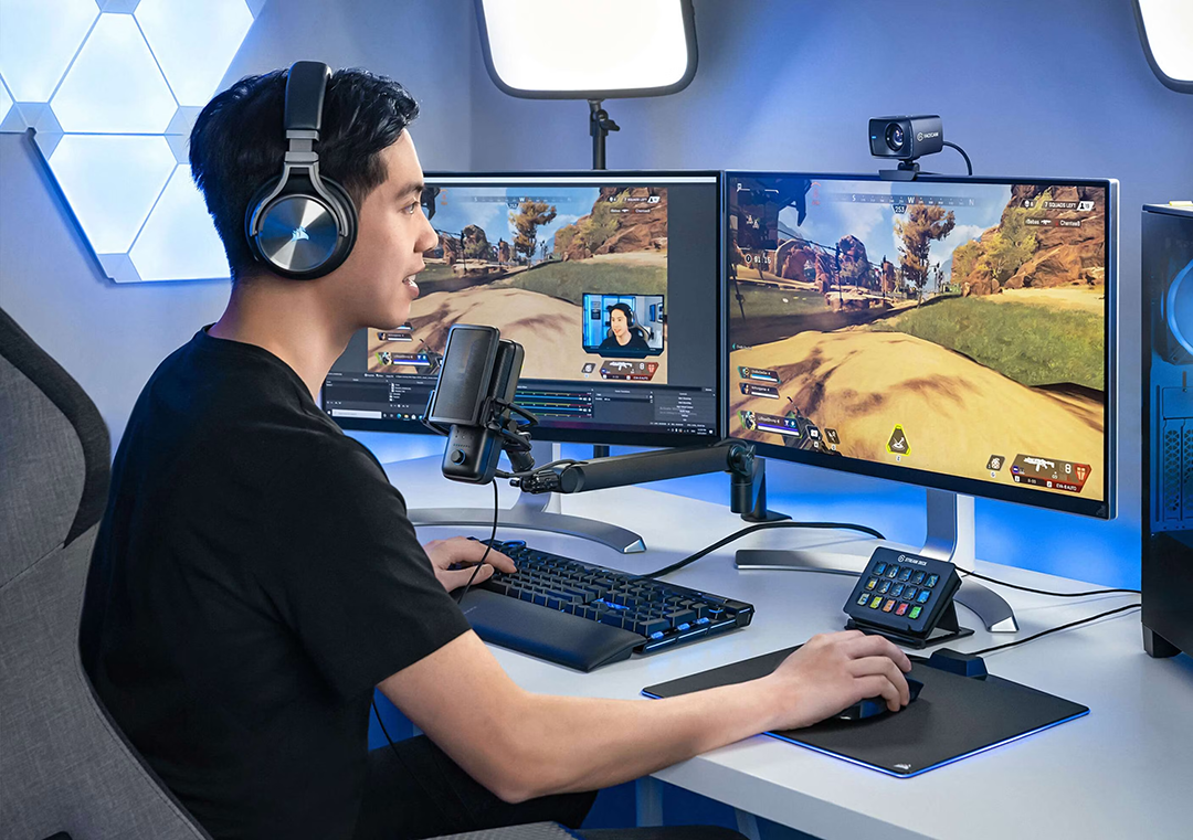 Egy fejhallgatós fiatalember videójátékozik két monitoron, mikrofonnal és stream deckkel az asztalán.
