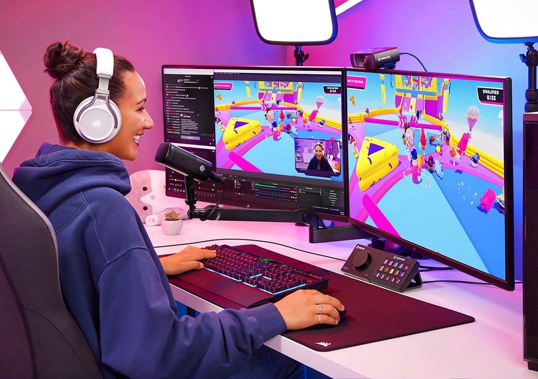 Egy fehér fejhallgatós nő színes videojátékot közvetít két monitoron.