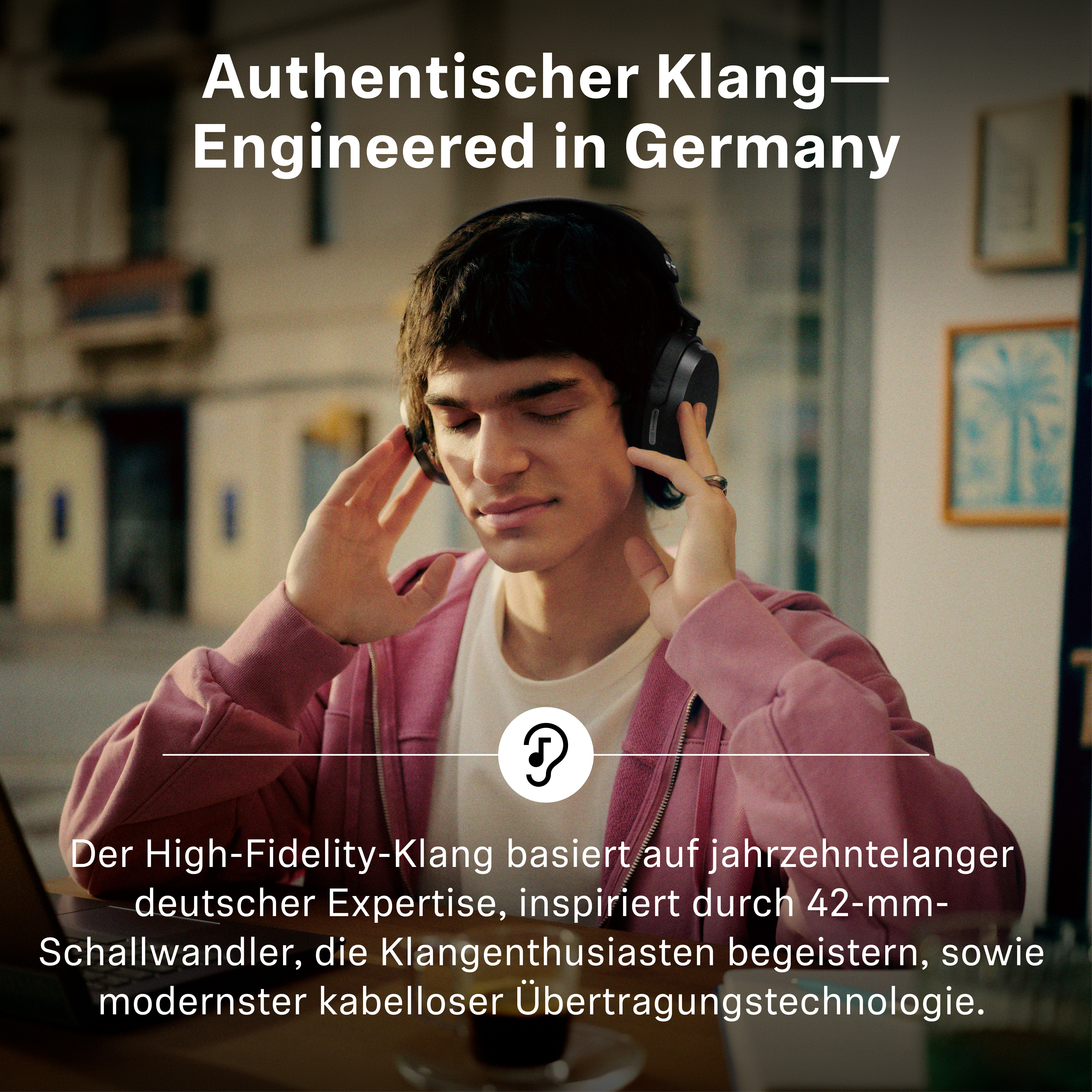 Ein junger Mann mit geschlossenen Augen trägt große schwarze Kopfhörer in einem Innenraum mit Werbetext.