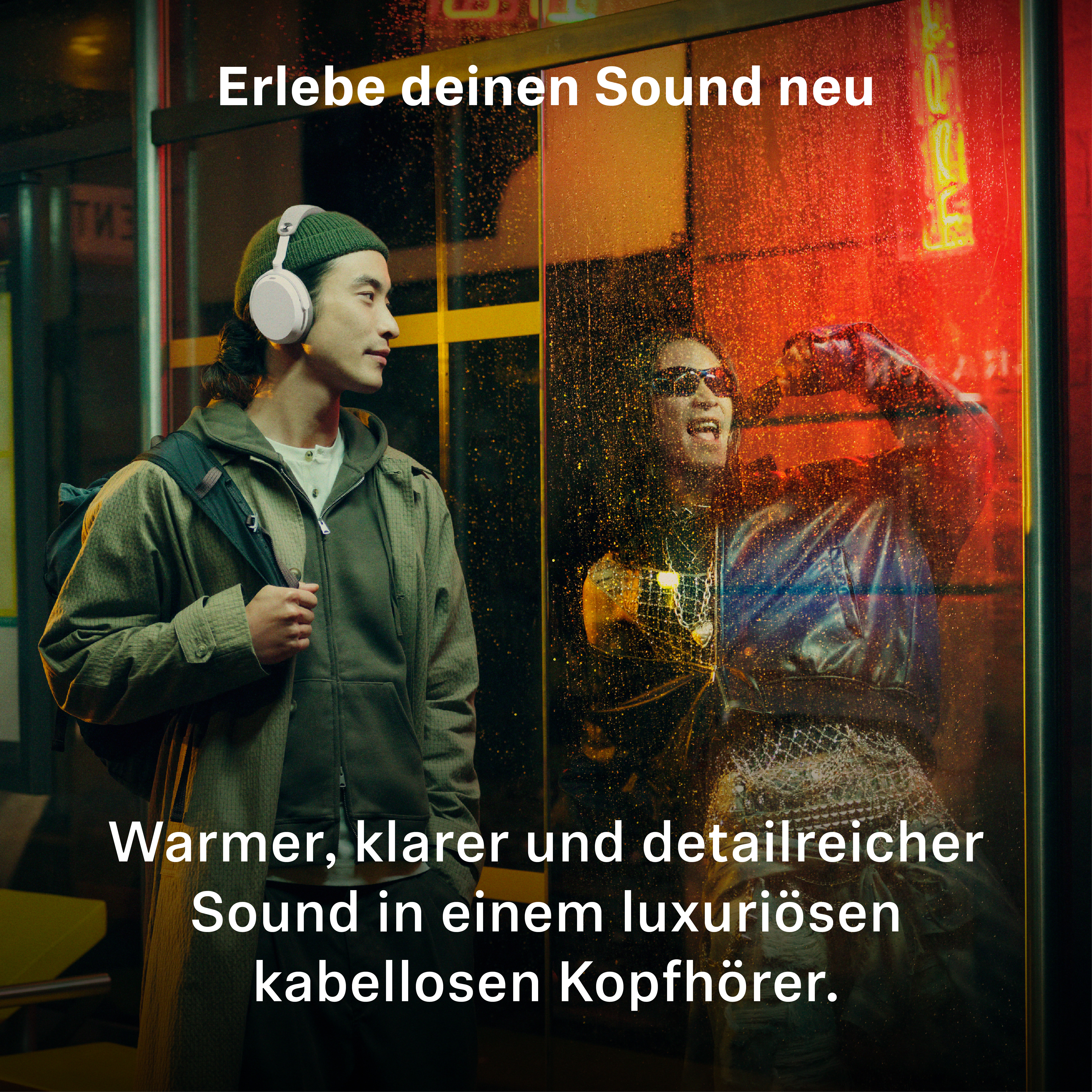 Ein Mann mit Mütze und weißen Kopfhörern steht vor einer verglasten Wand, dahinter eine leuchtend rote Szene.