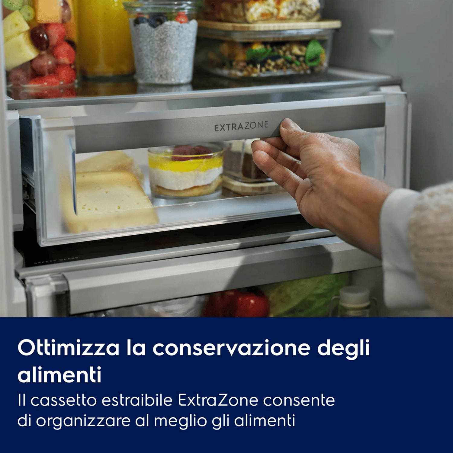 Una mano apre il cassetto ExtraZone di un frigorifero, pieno di alimenti come formaggio e dolci.