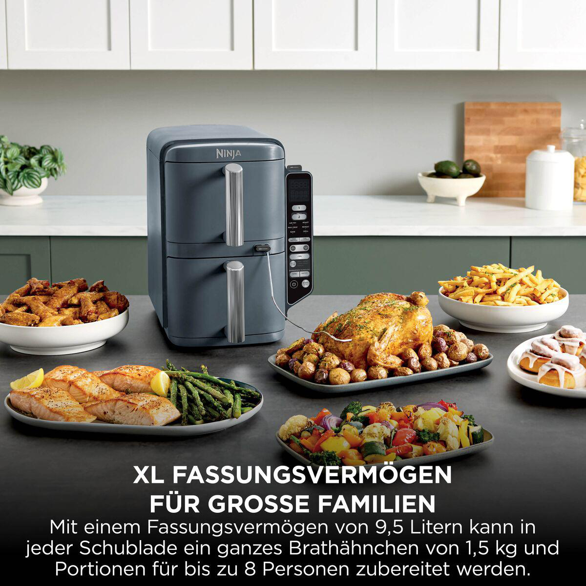 Ninja-Heißluftfritteuse auf der Arbeitsplatte, umgeben von Schüsseln mit gebratenem Hähnchen, Fisch und Gemüse.