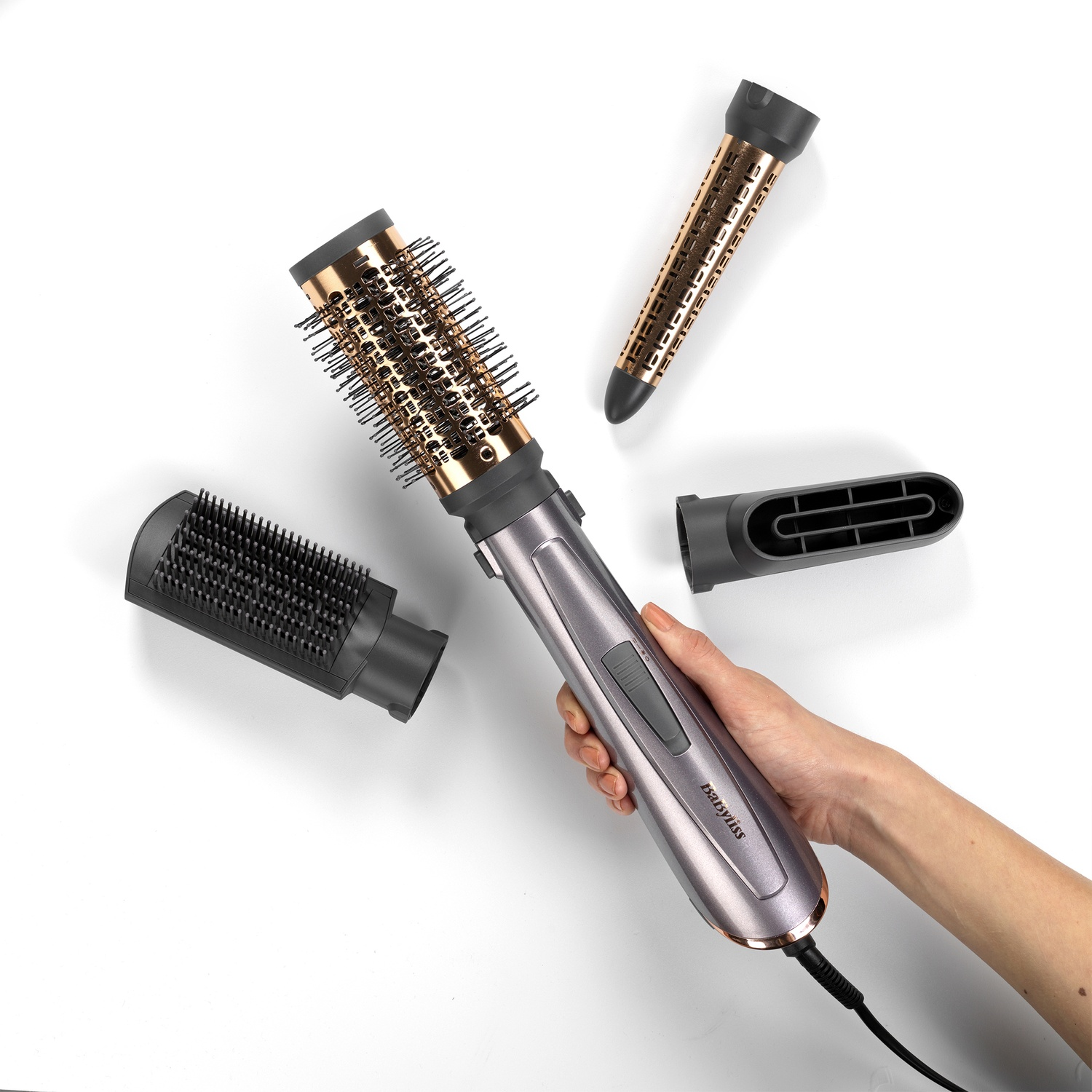 Una mano sostiene un styler per capelli grigio, circondato da tre diversi accessori su sfondo bianco.