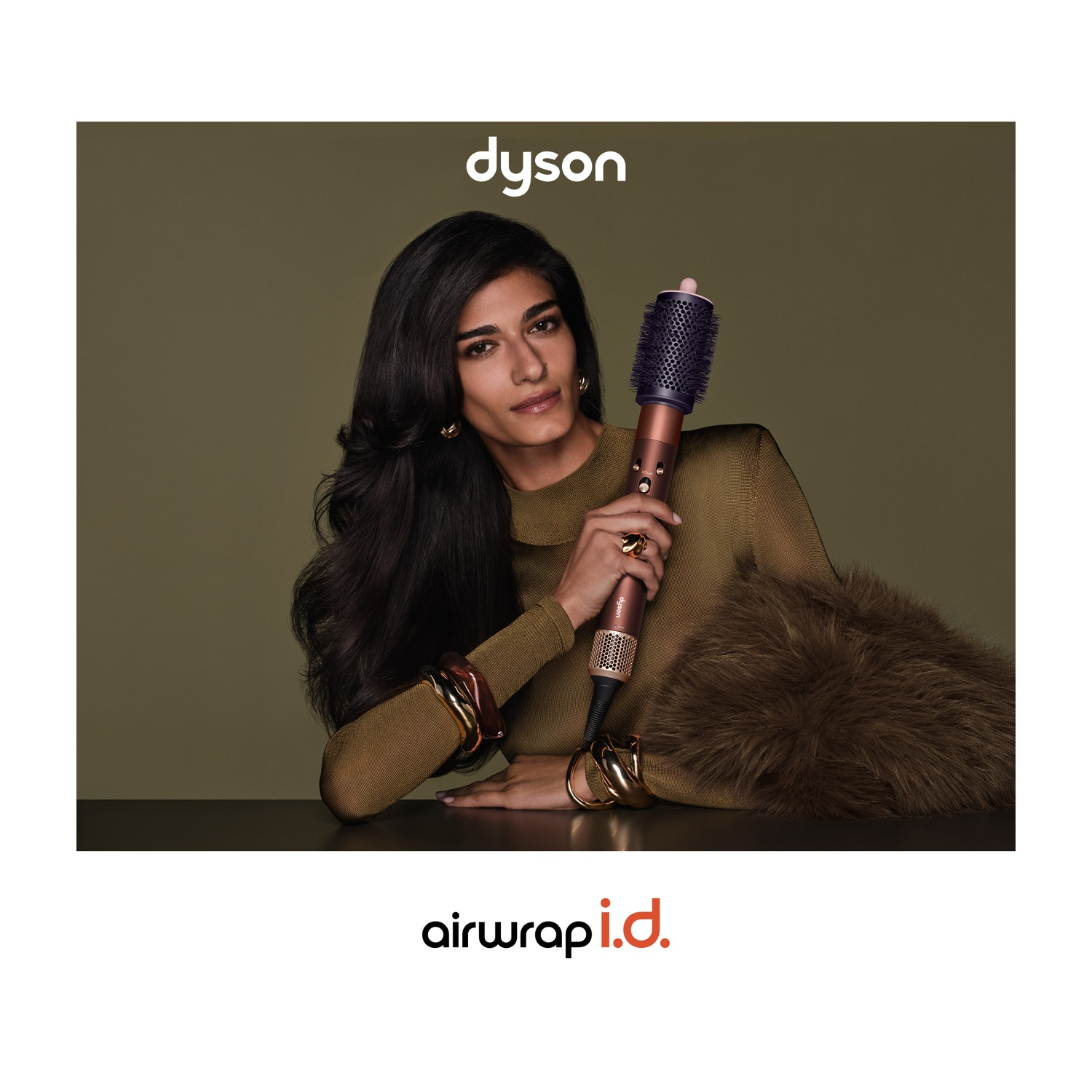 Una donna dai capelli scuri tiene un Dyson Airwrap su uno sfondo verde oliva.