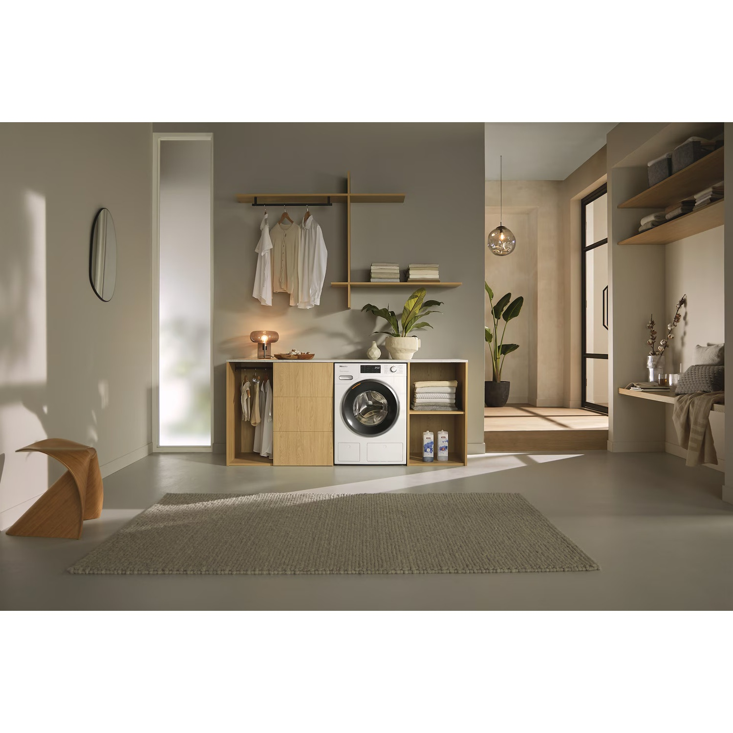 Een moderne bijkeuken met witte wasmachine, houten planken, hangende kleding en een vloerkleed.