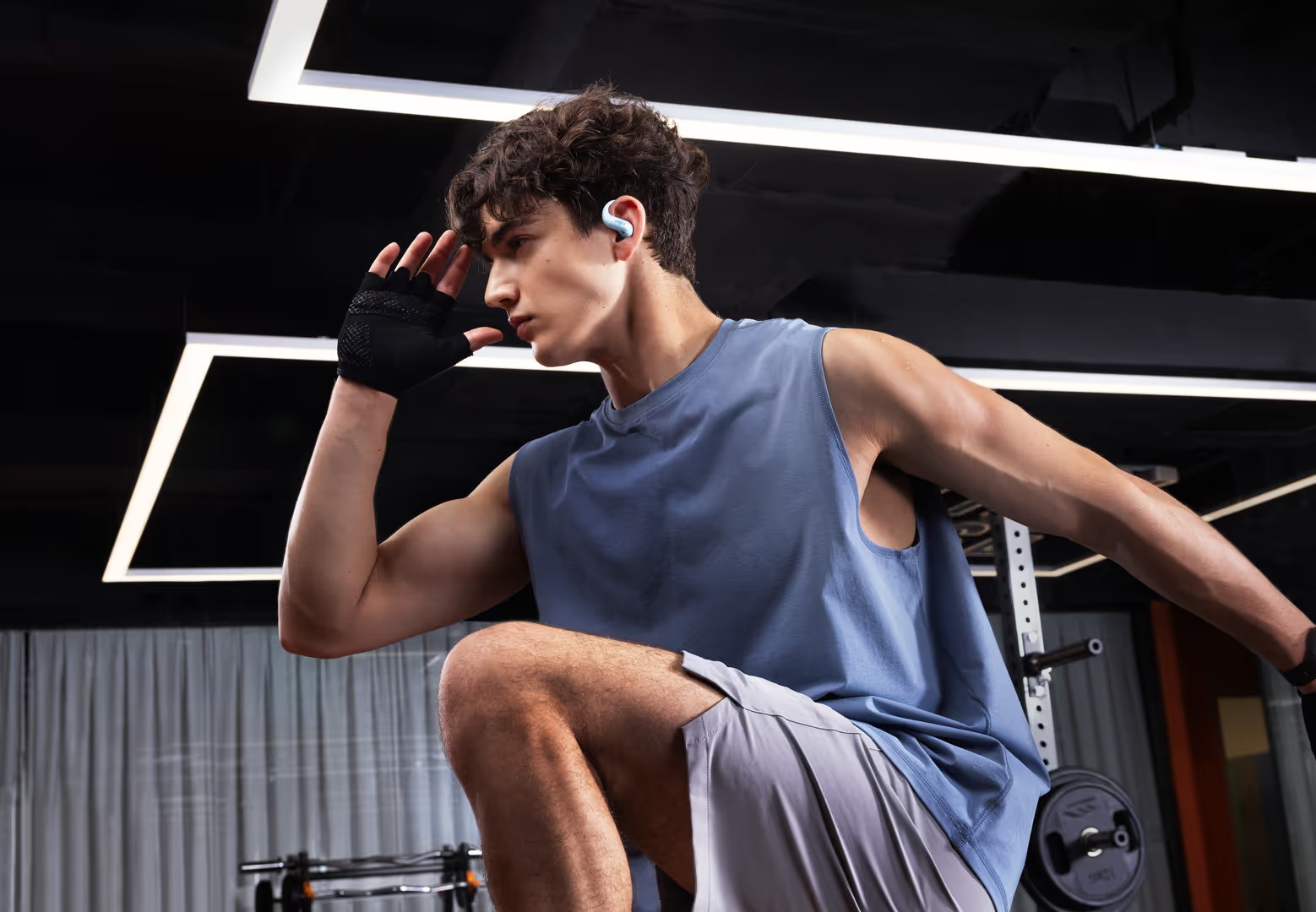 Ein junger Mann im blauen Sportshirt trainiert im modernen Fitnessstudio mit Kopfhörern.