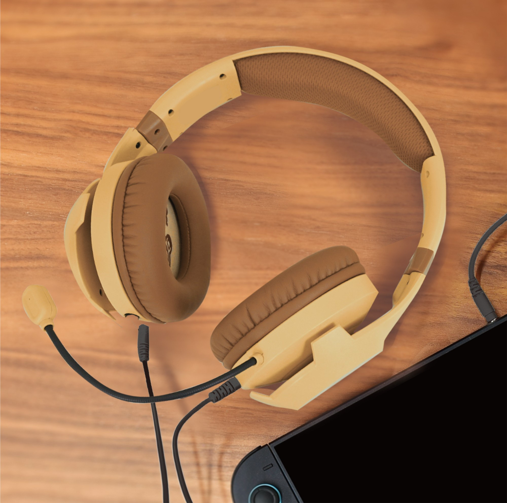 Cuffie da gioco con filo beige e marrone su superficie di legno accanto a un dispositivo.
