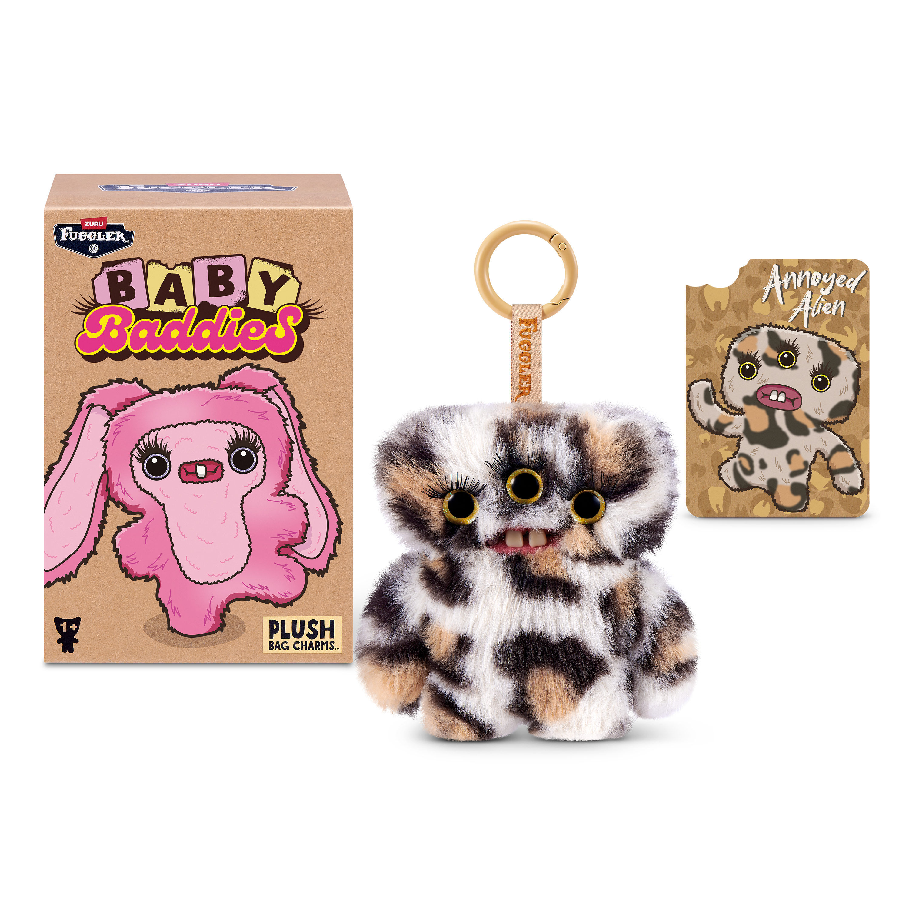 Un peluche Fuggler Baby Baddies de tres ojos con dientes humanos, su caja y una tarjeta Annoyed Alien.
