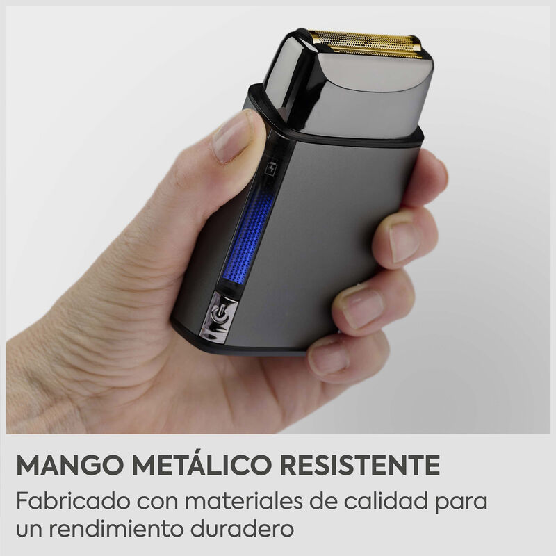 Una mano sostiene una afeitadora eléctrica gris con cuchilla dorada y luz azul.