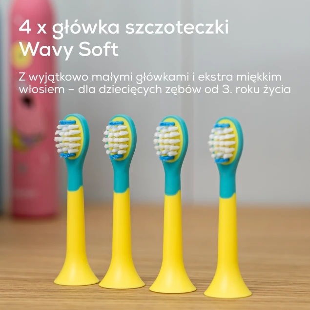 Cztery żółto-turkusowe główki szczoteczek dla dzieci stoją na drewnianej powierzchni.