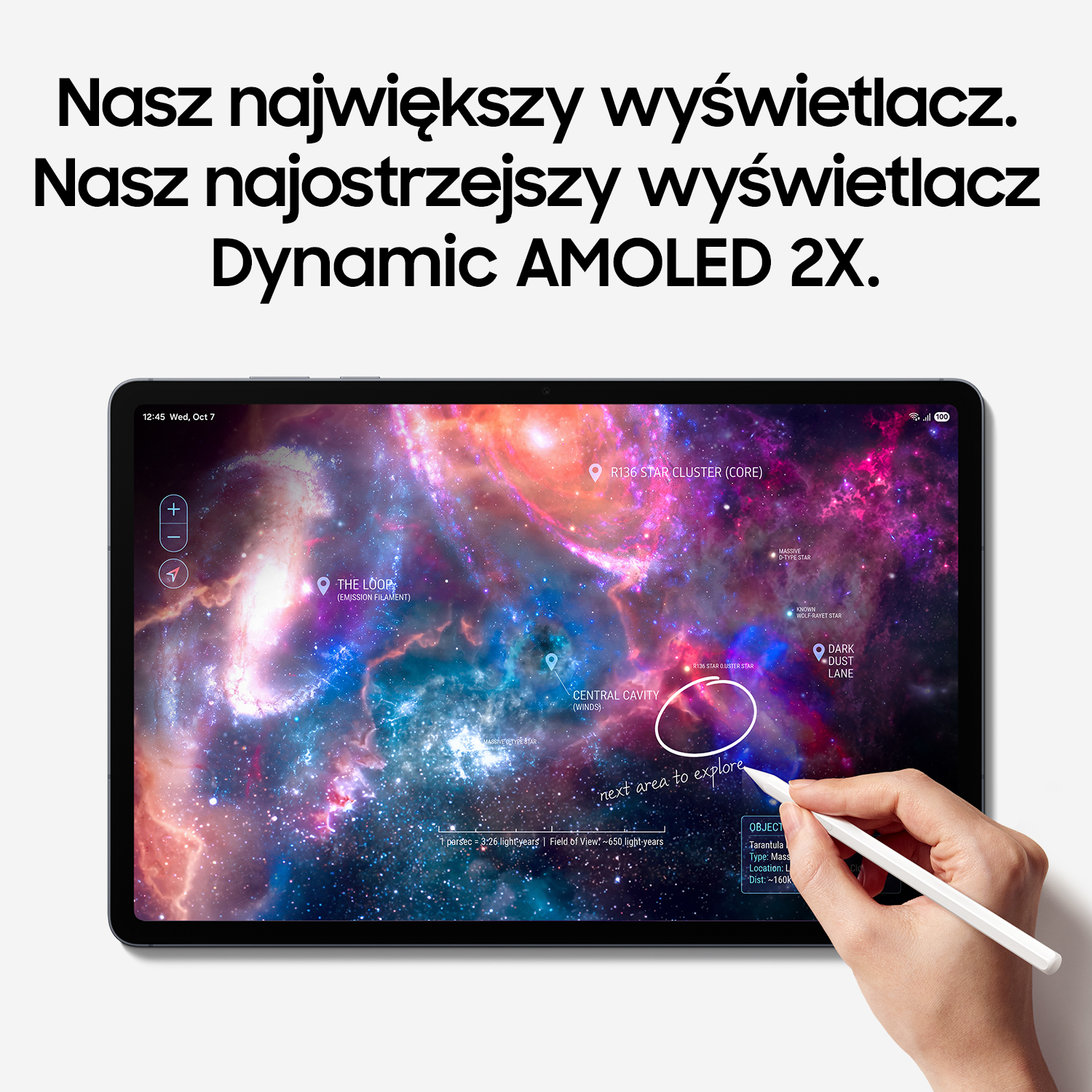 Tablet z jasnym ekranem przedstawia galaktykę, a dłoń pisze na nim za pomocą rysika.