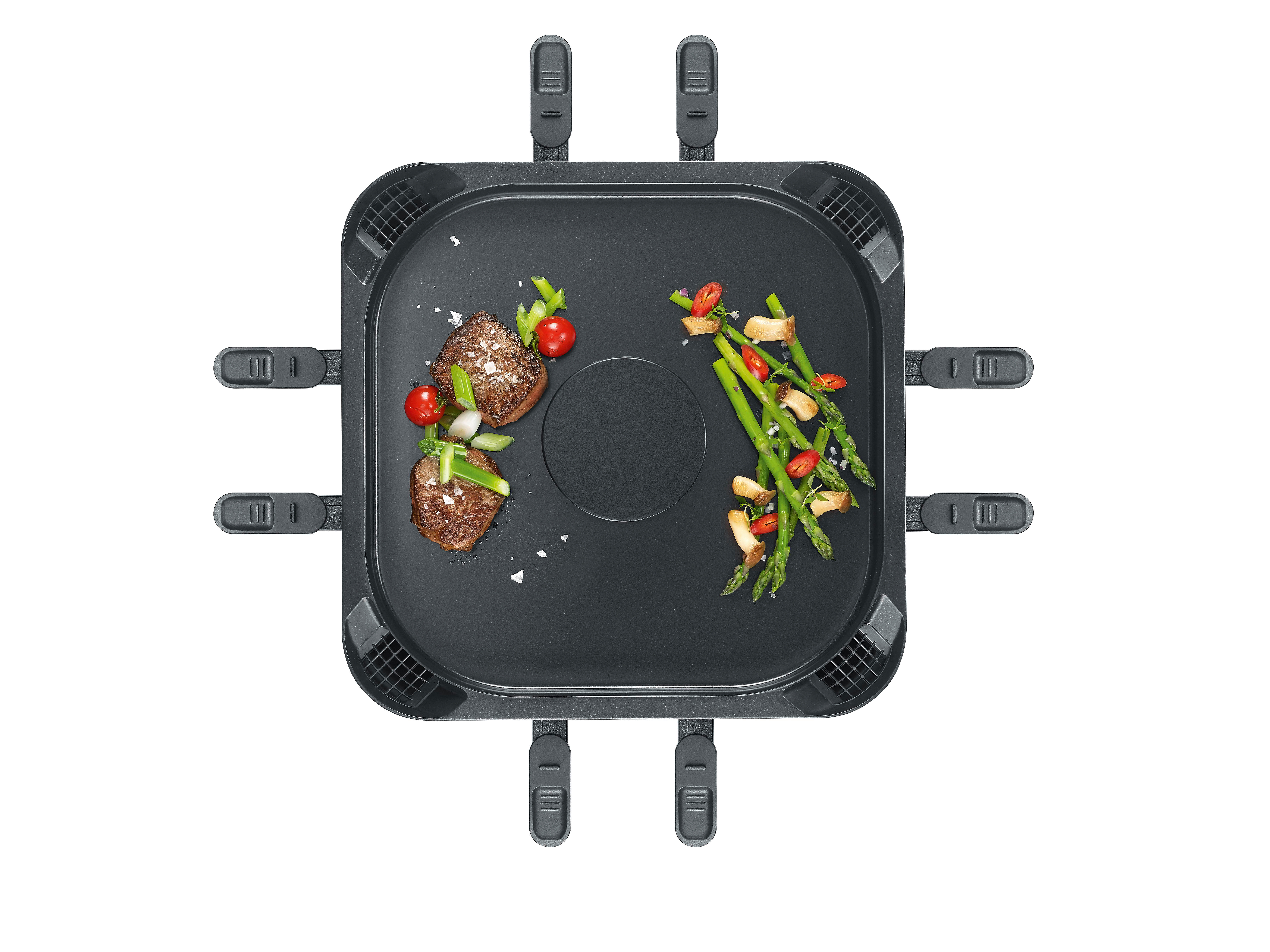 Ein schwarzer Raclette-Grill von oben mit Fleisch, Spargel und Tomaten auf der Grillplatte.