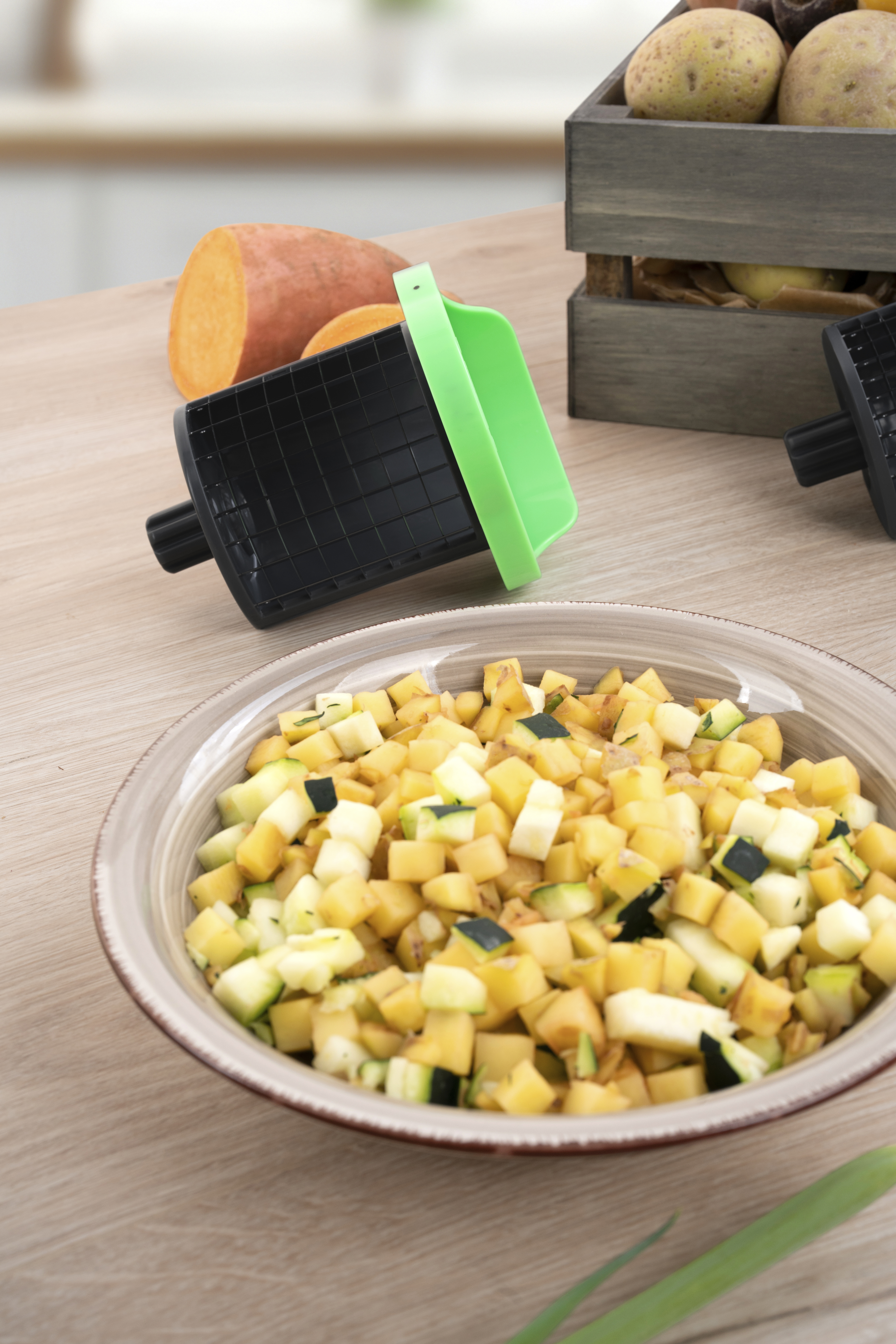 Gemüseschneider mit grüner Klinge und Schüssel mit gewürfeltem Gemüse.