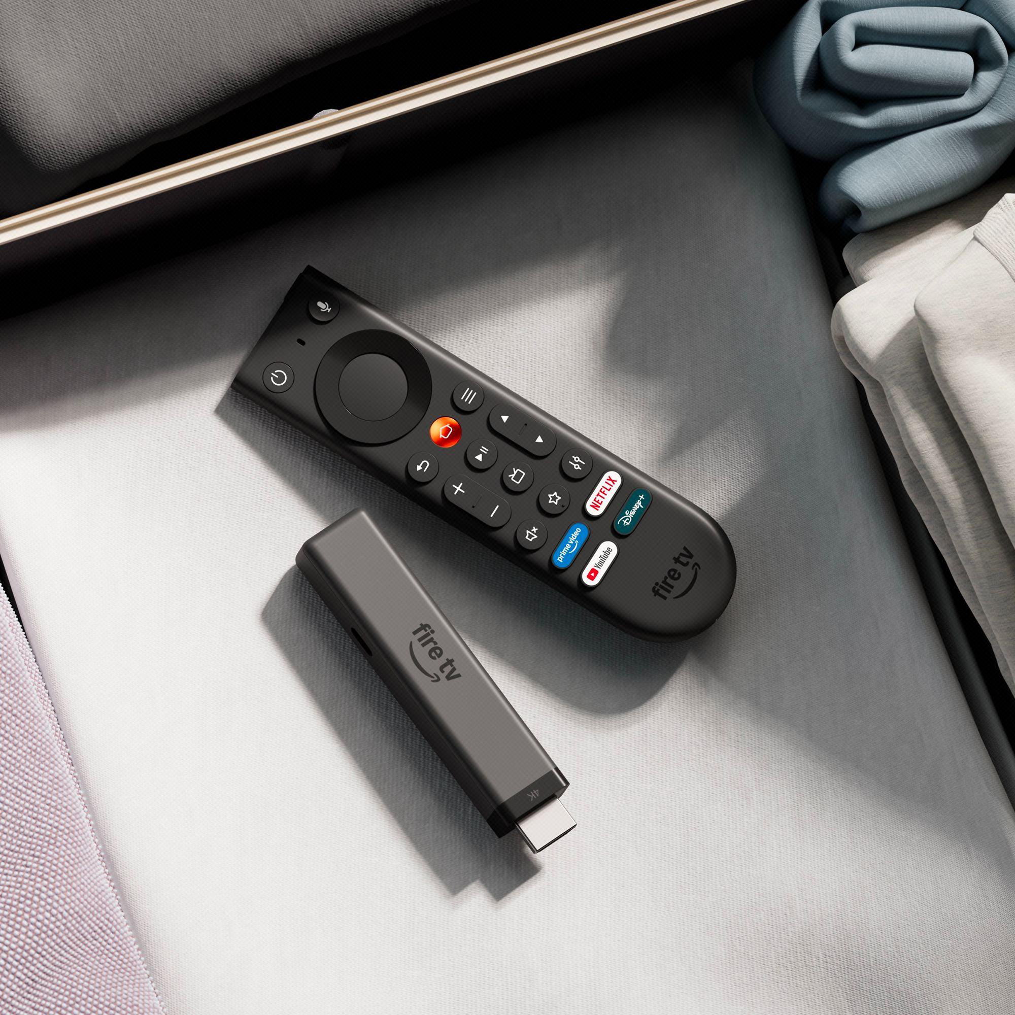 Ein Fire TV Stick mit Fernbedienung liegt neben Kleidung auf einem Bett.