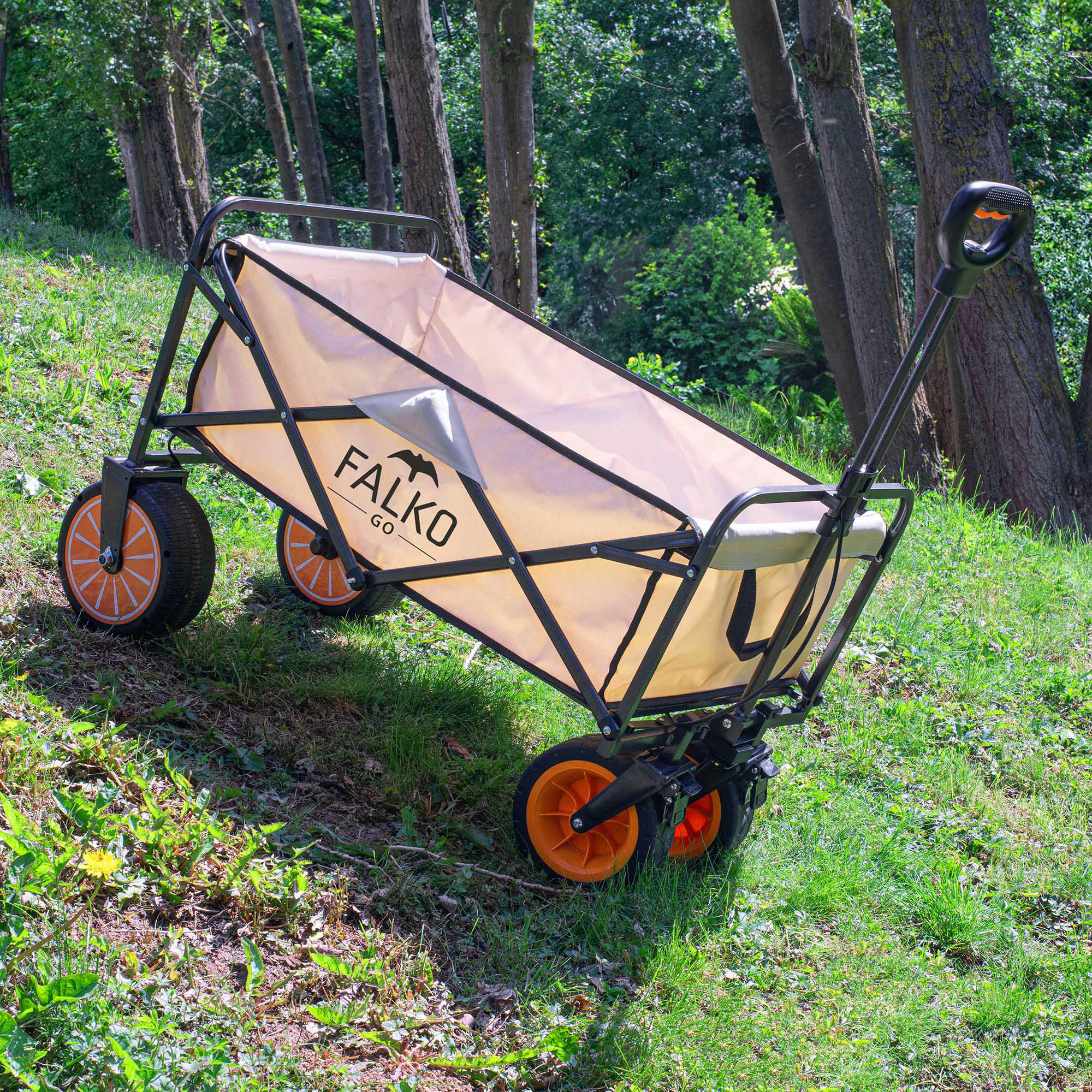 Ein beiger Faltoirradwagen mit orangen Rädern steht auf einer grünen Waldwiese.