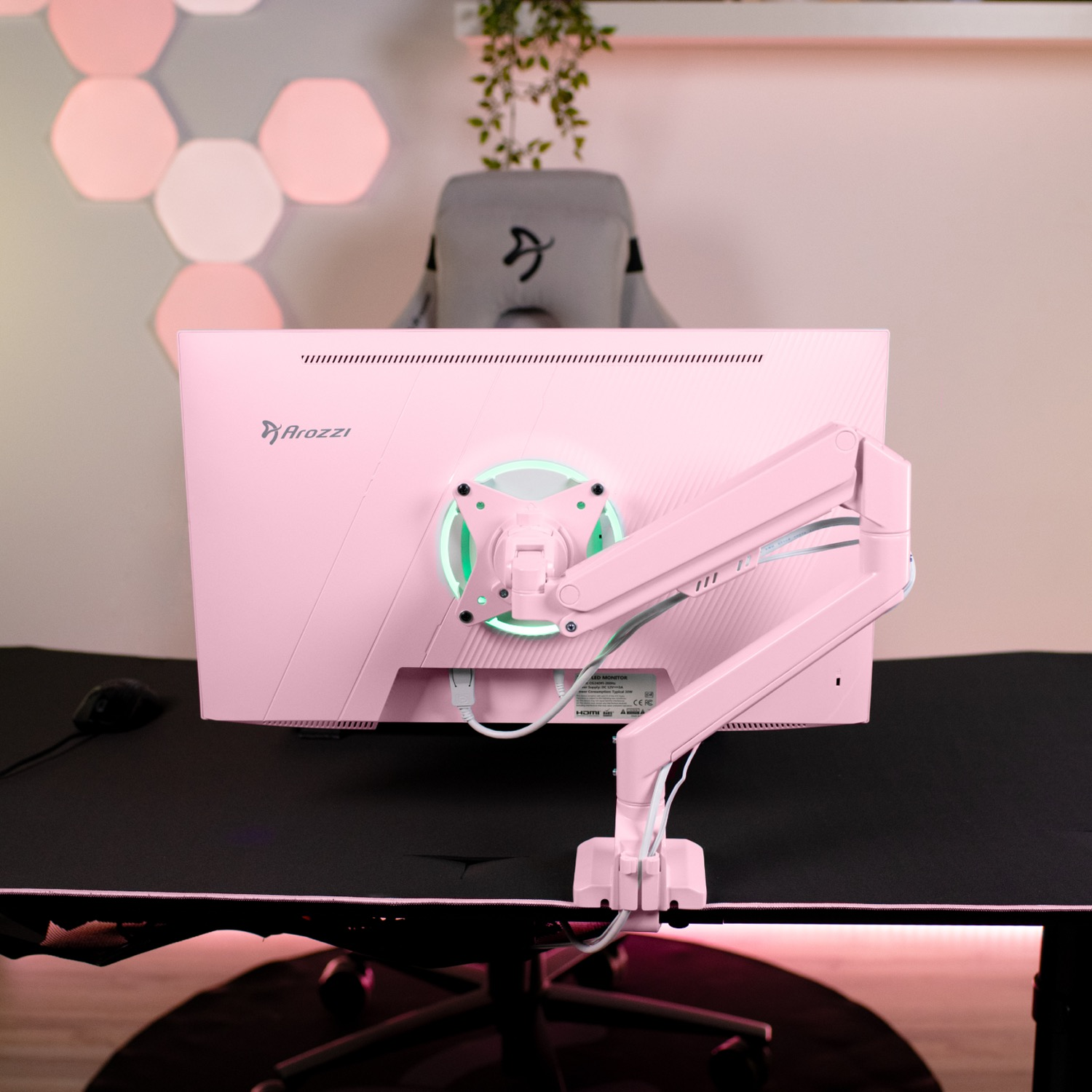 Ein pinker Arozzi-Monitor auf einem Arm an einem Schreibtisch mit Gaming-Stuhl und Wandbeleuchtung.