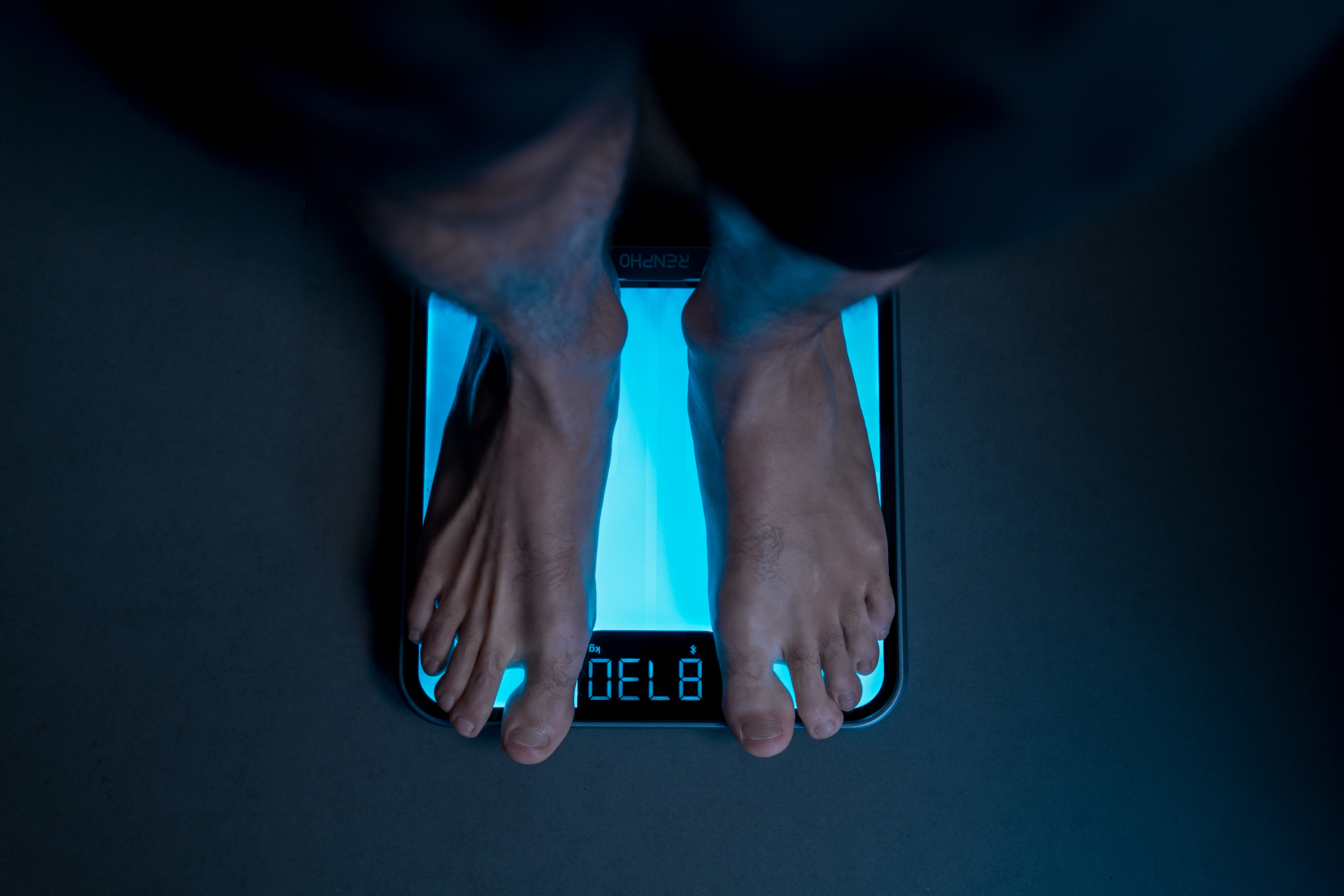 Persona descalza de pie sobre una báscula de baño digital azul brillante.