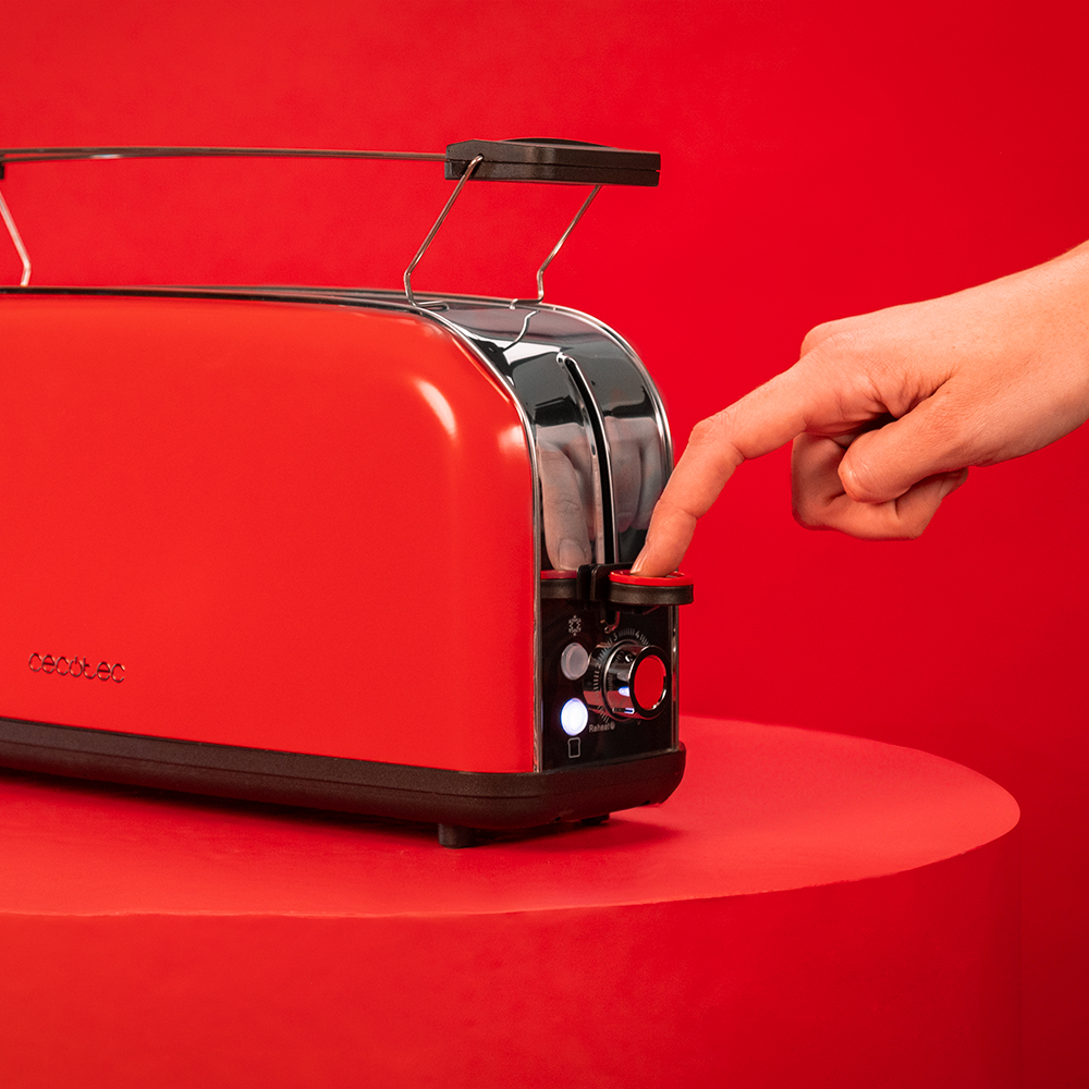 Una mano presiona la palanca de una tostadora roja en una mesa roja contra un fondo rojo.