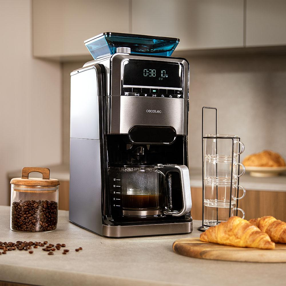 Cafetera moderna en una encimera de cocina con granos de café, tazas y cruasanes.