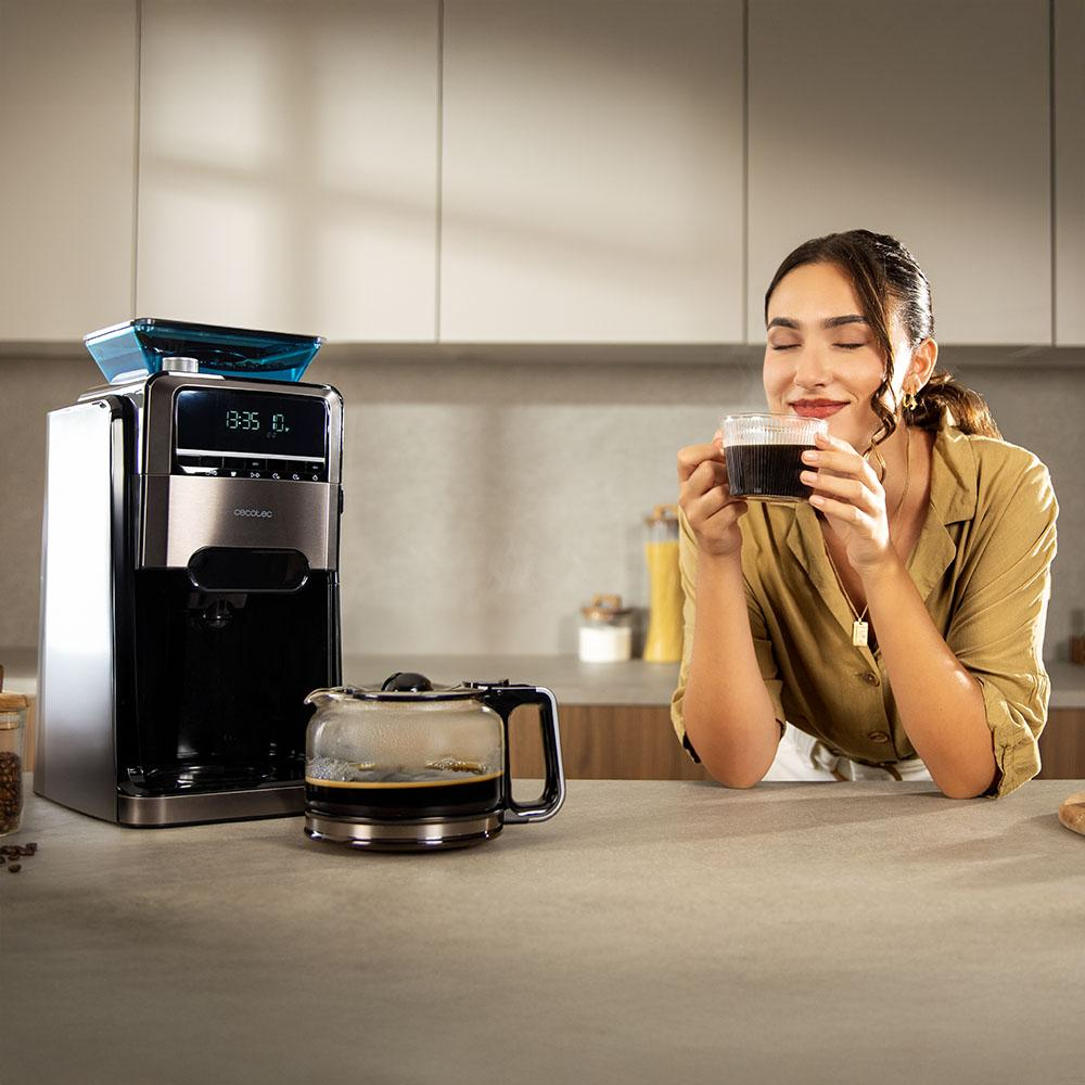 Una mujer disfruta del aroma del café de una taza junto a una cafetera en una cocina moderna.