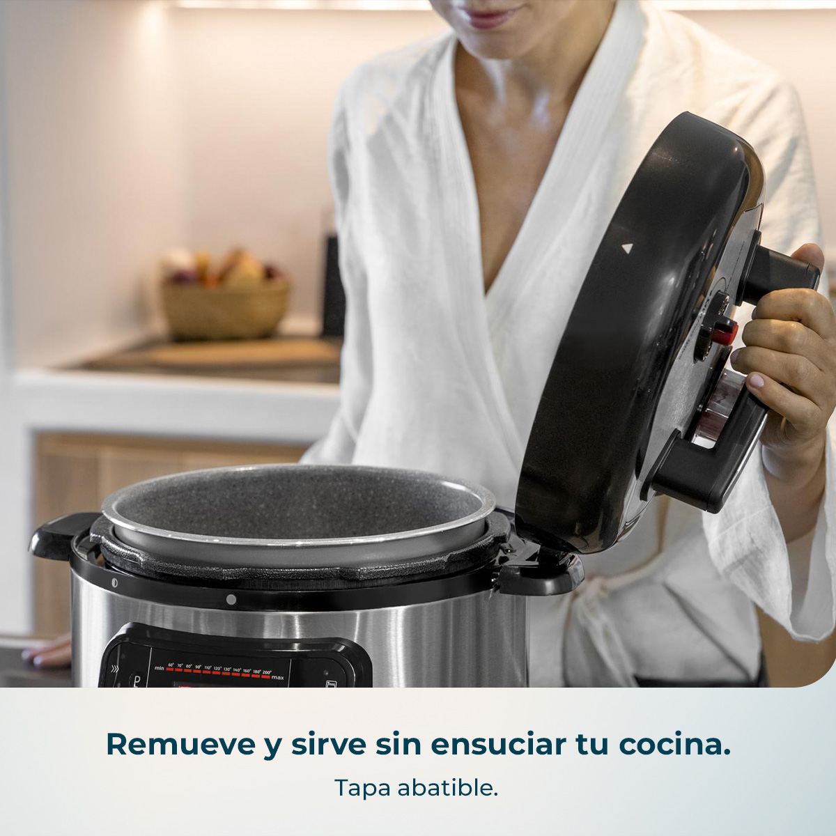 Una mujer con ropa blanca abre la tapa de una moderna olla multicocina de acero inoxidable en una cocina.