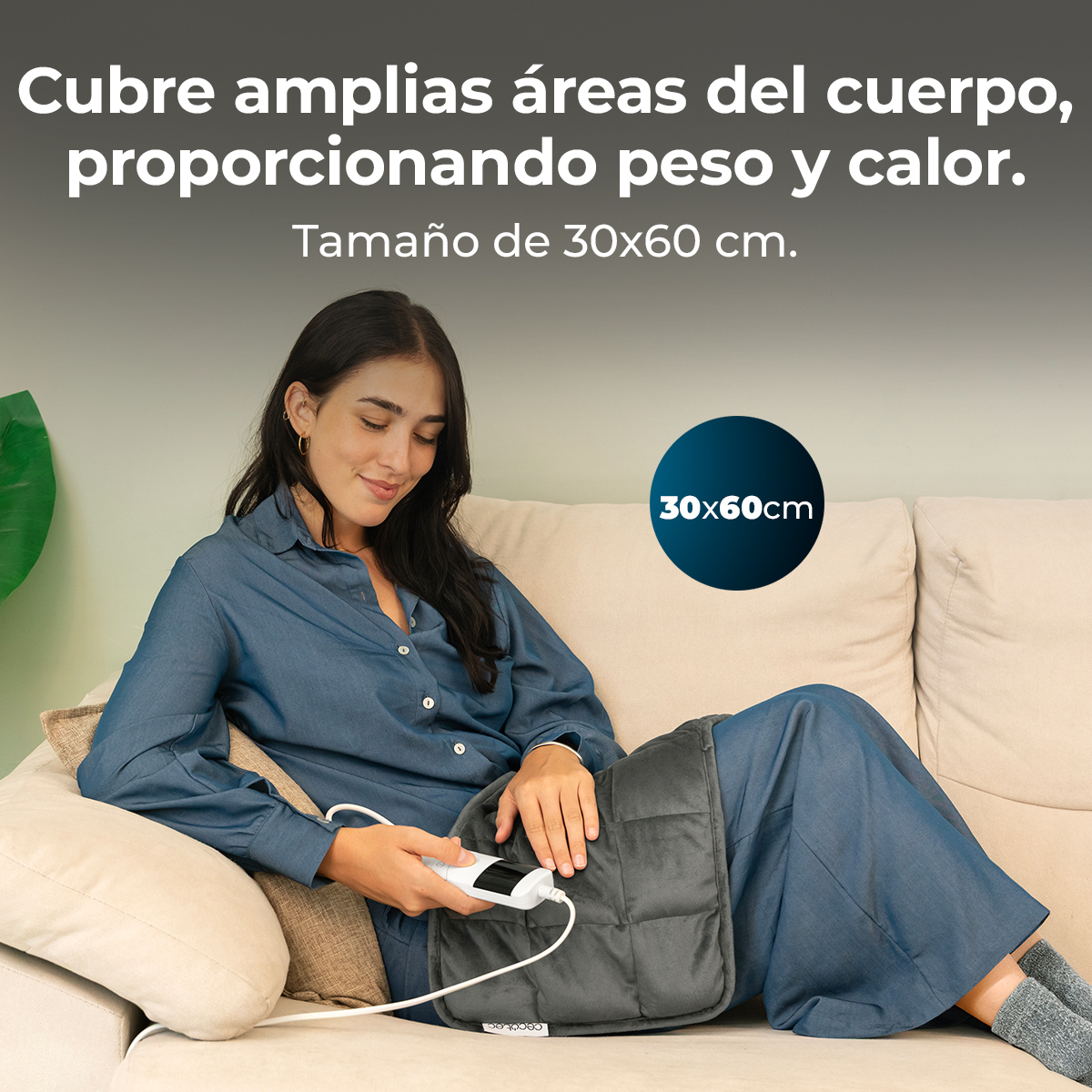 Una mujer está sentada en un sofá, sosteniendo una almohadilla térmica eléctrica gris.