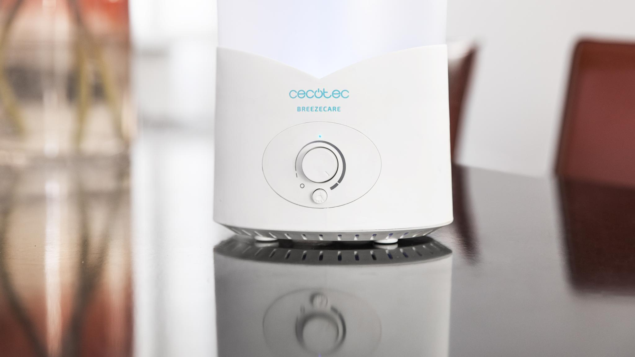 Un humidificador blanco Cecotec Breezecare sobre una mesa oscura, reflejándose en la superficie.
