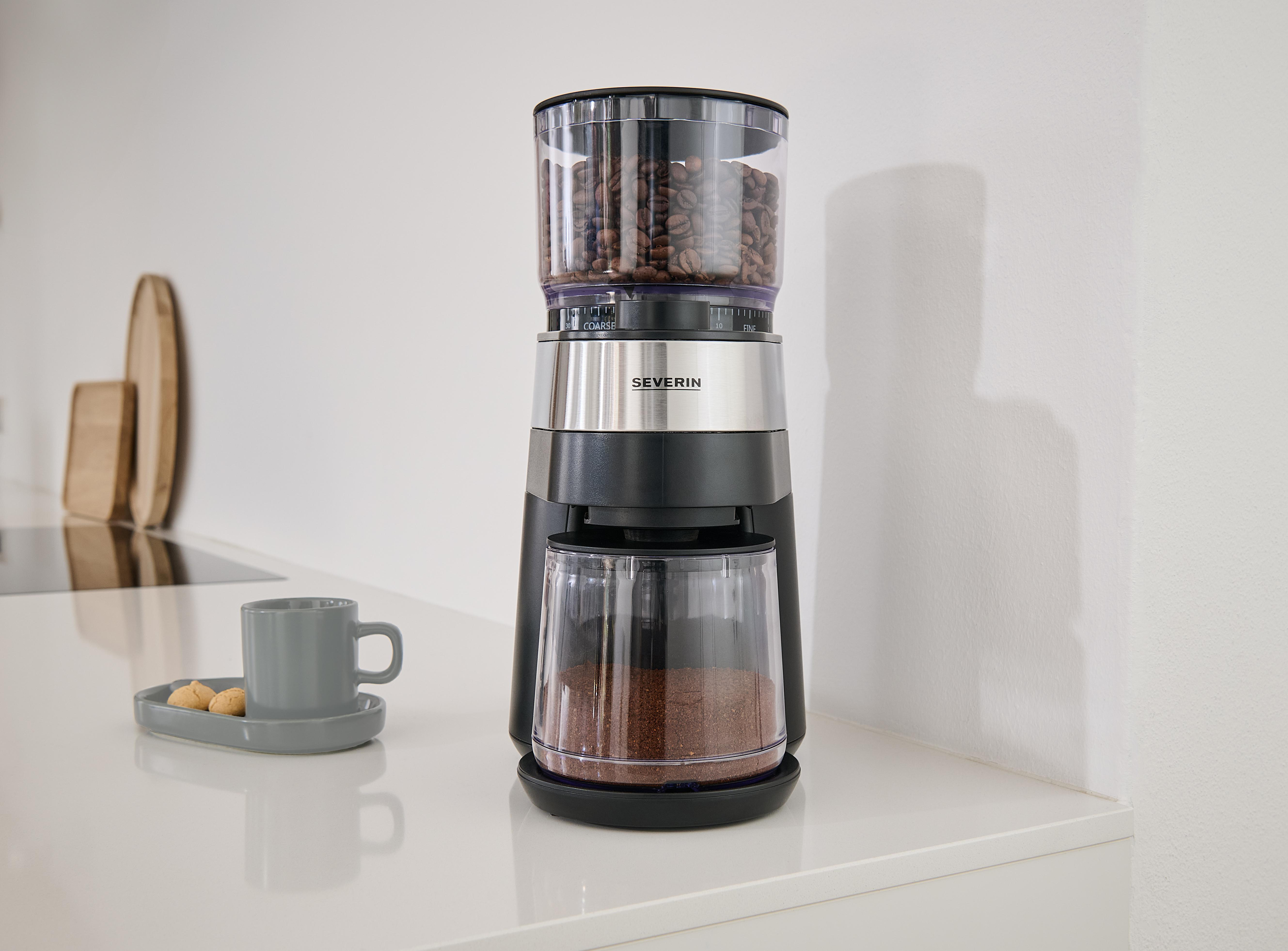 Eine schwarze Severin Kaffeemühle mit Bohnen und Pulver steht auf einer weißen Theke neben einer grauen Tasse.