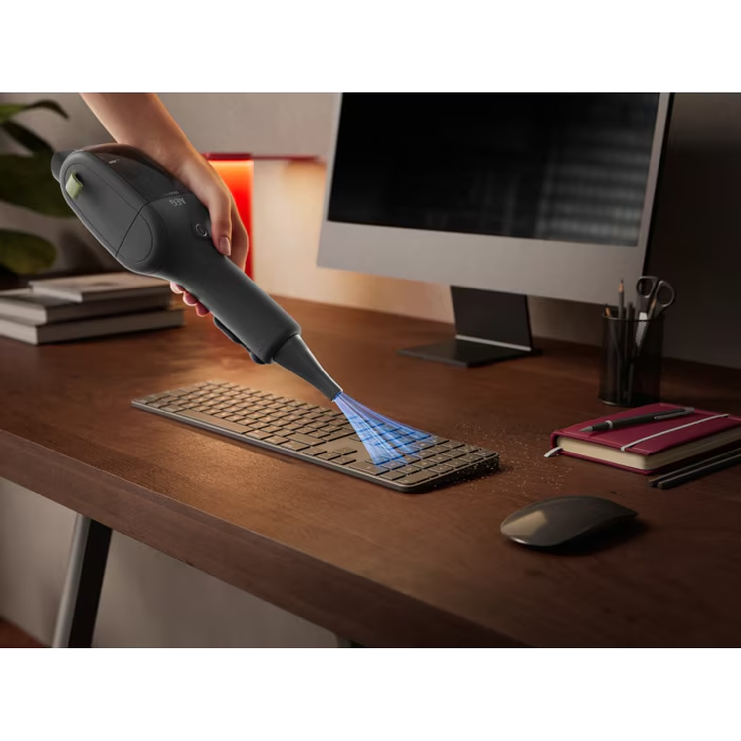 Handstofzuiger zuigt kruimels van een computertoetsenbord op een houten bureau.