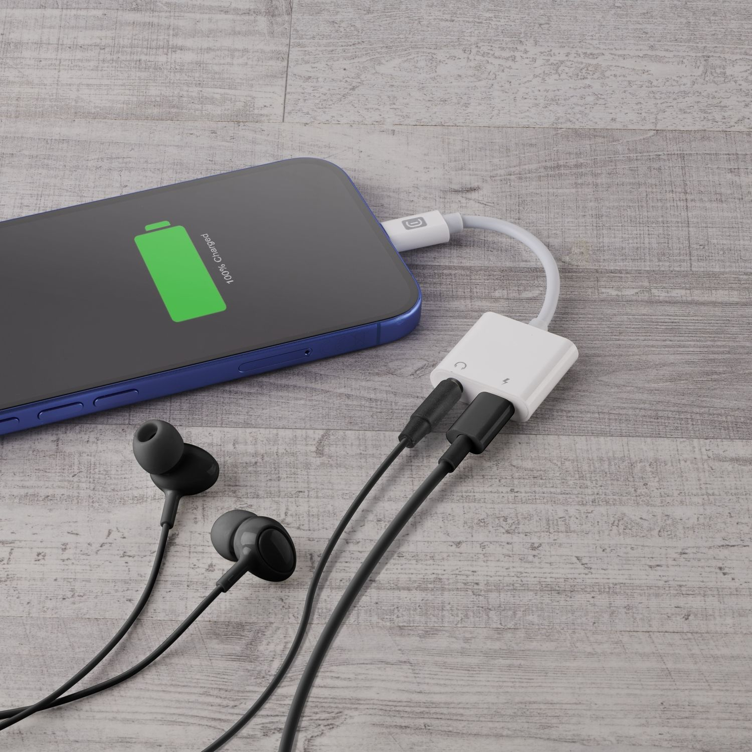 Un smartphone azul en una mesa de madera muestra una batería verde cargando, conectado a un adaptador blanco.