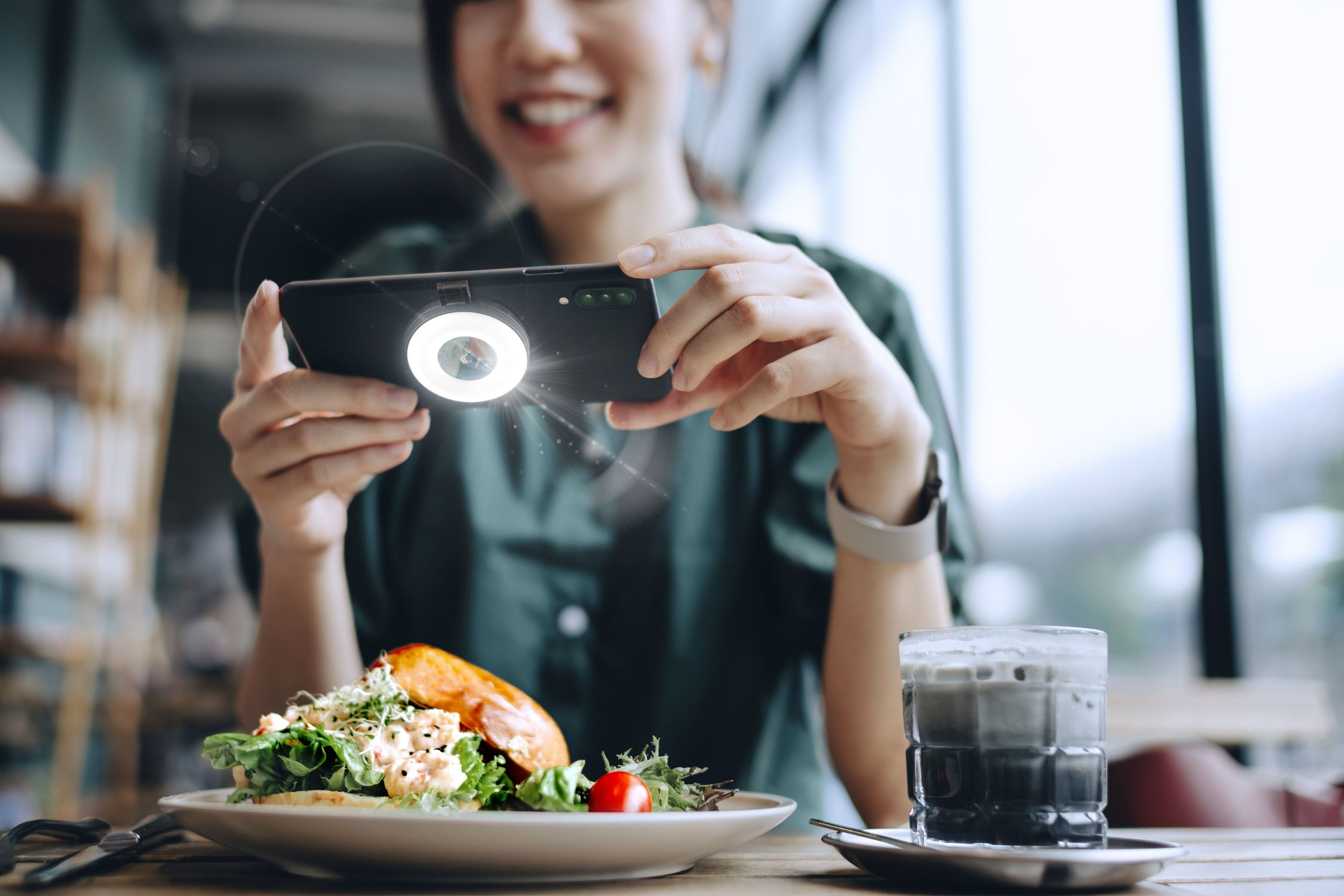 Una mujer toma una foto de una ensalada con su teléfono y luz de anillo.