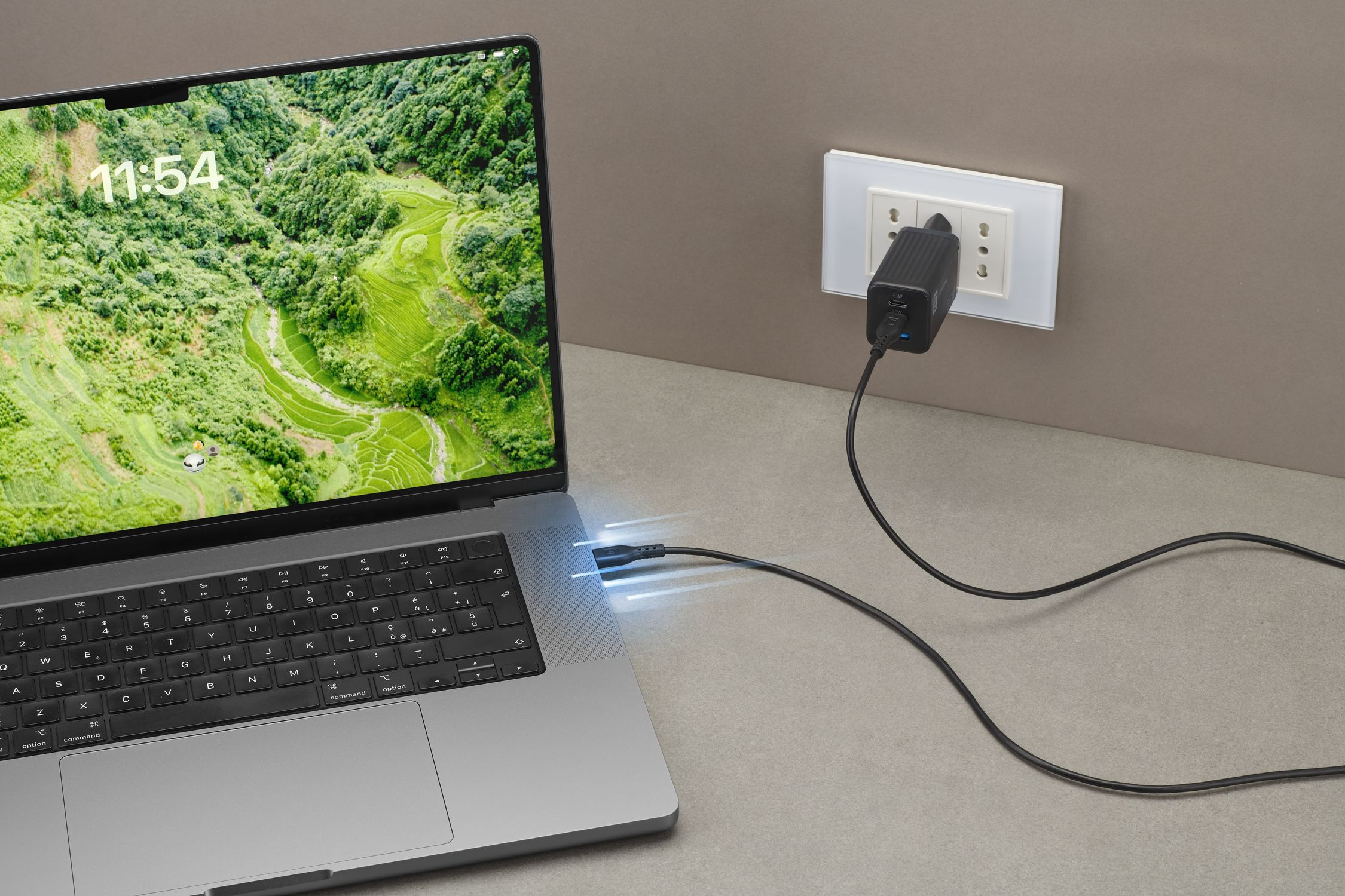 Un ordenador portátil gris está conectado a un enchufe de pared mediante un cable de carga negro.