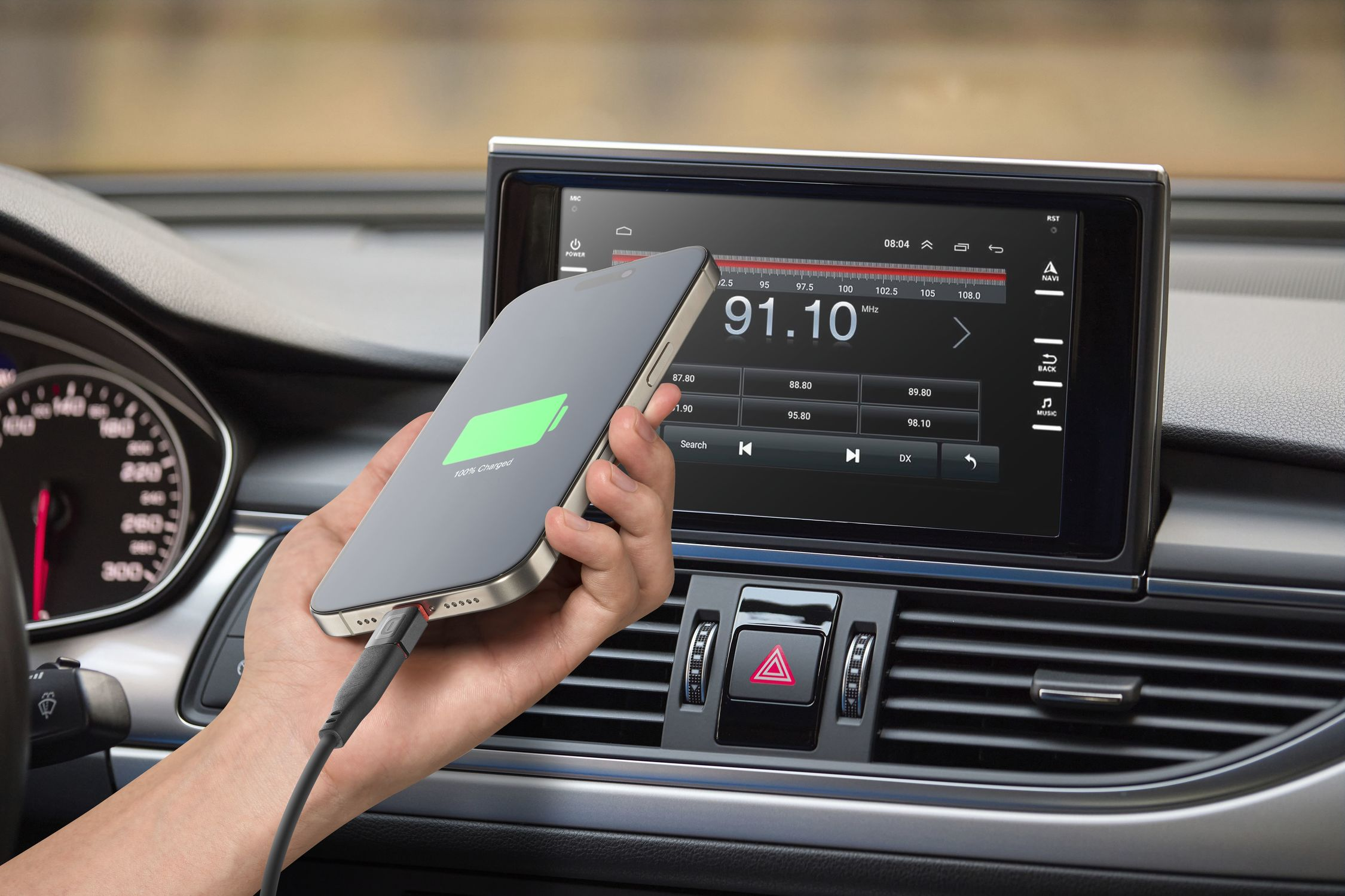 Una mano sostiene un teléfono con icono de carga verde en el coche, con pantalla multimedia al fondo.