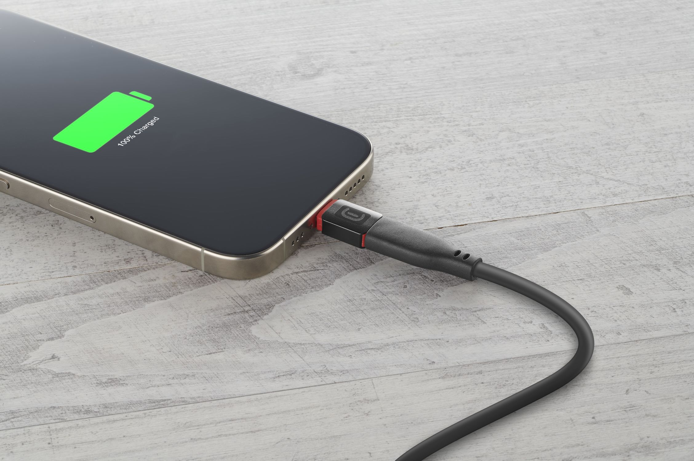Un teléfono inteligente se carga en una mesa de madera, la pantalla muestra un icono de batería verde.