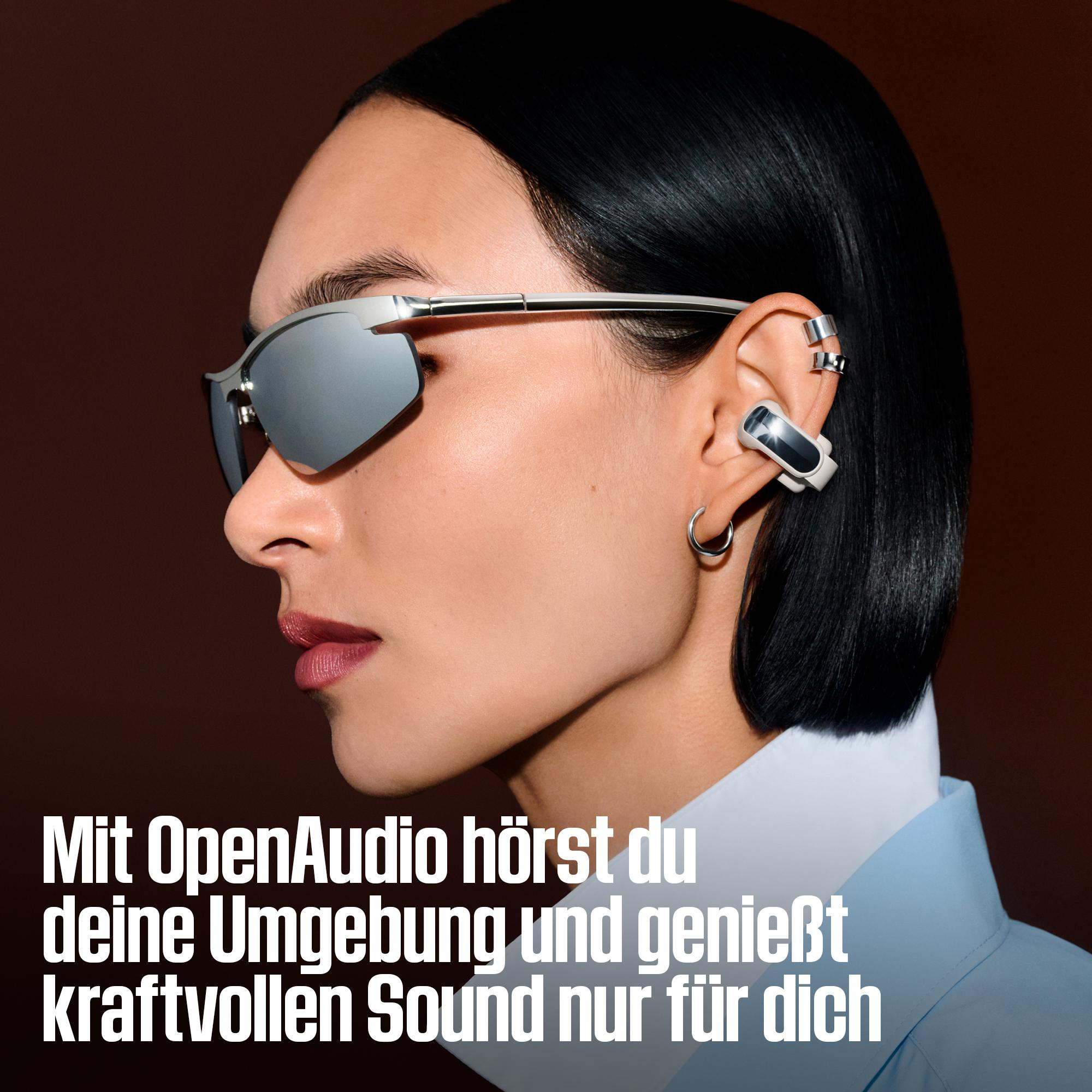 Frau mit silberner Sonnenbrille und modernem Ohrhörer vor braunem Hintergrund.