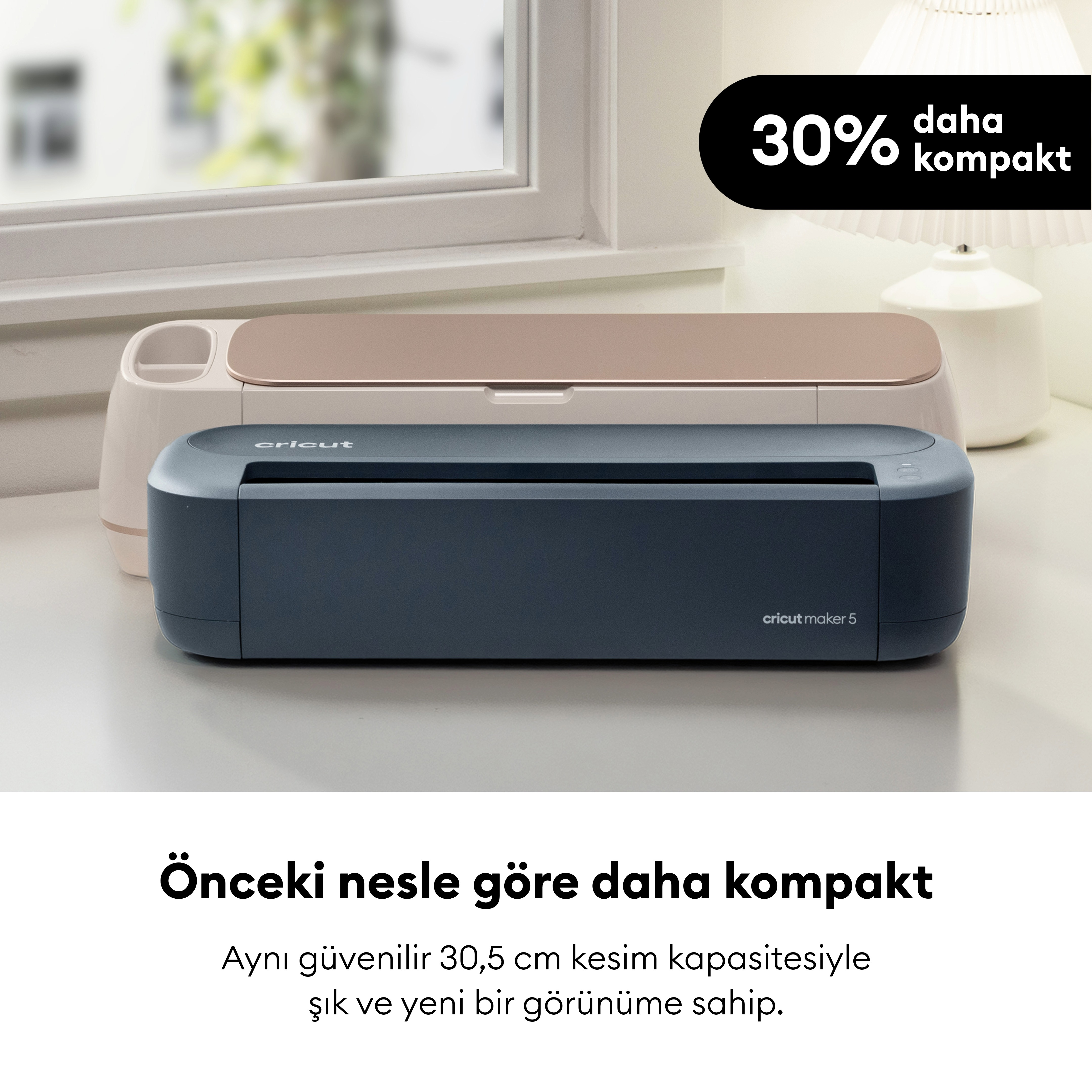 Bej ve koyu mavi renkli iki Cricut kesim makinesi pencere önündeki masada duruyor.