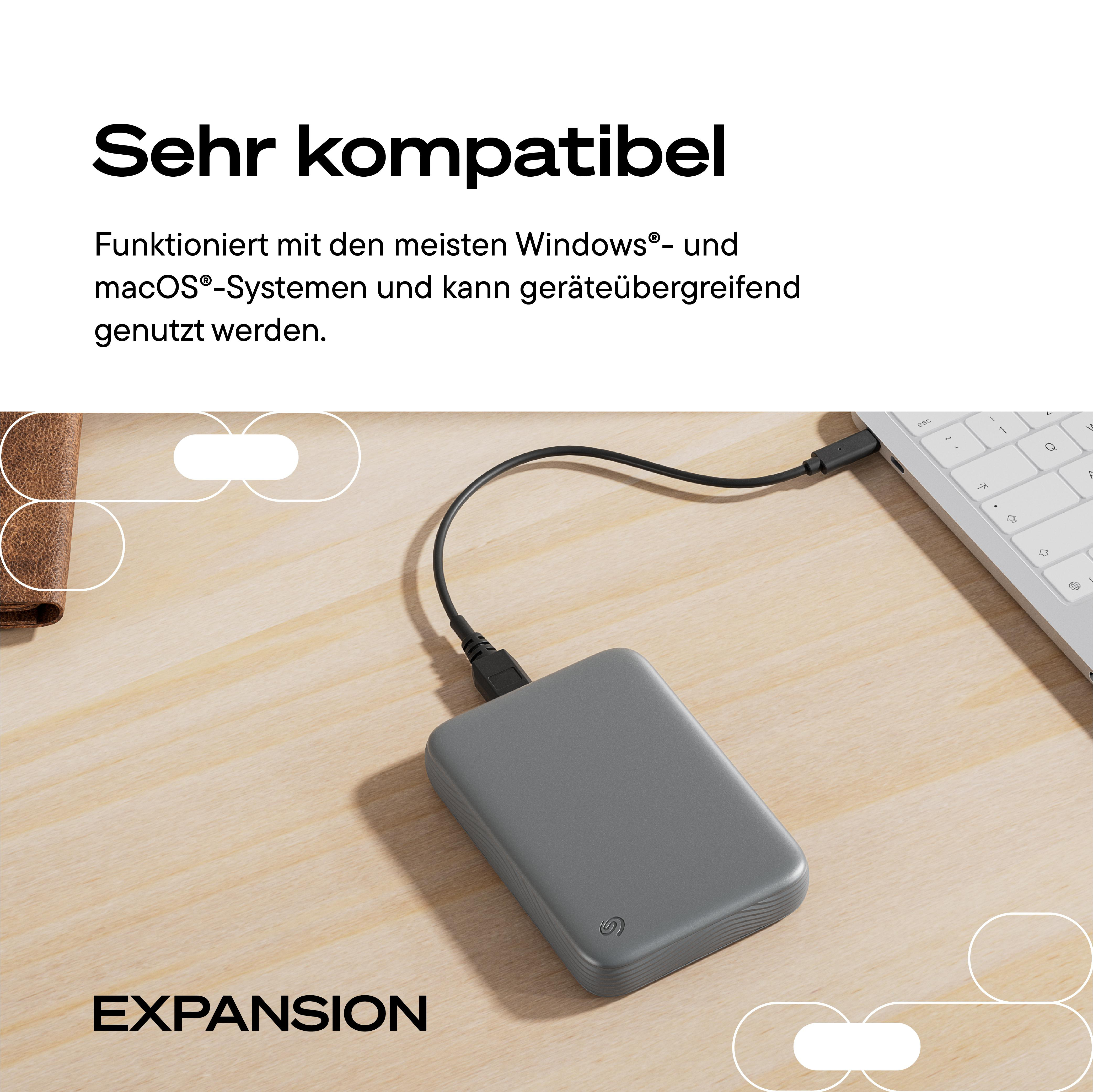 Graue Seagate Expansion Festplatte auf Holztisch, verbunden mit einem Laptop.