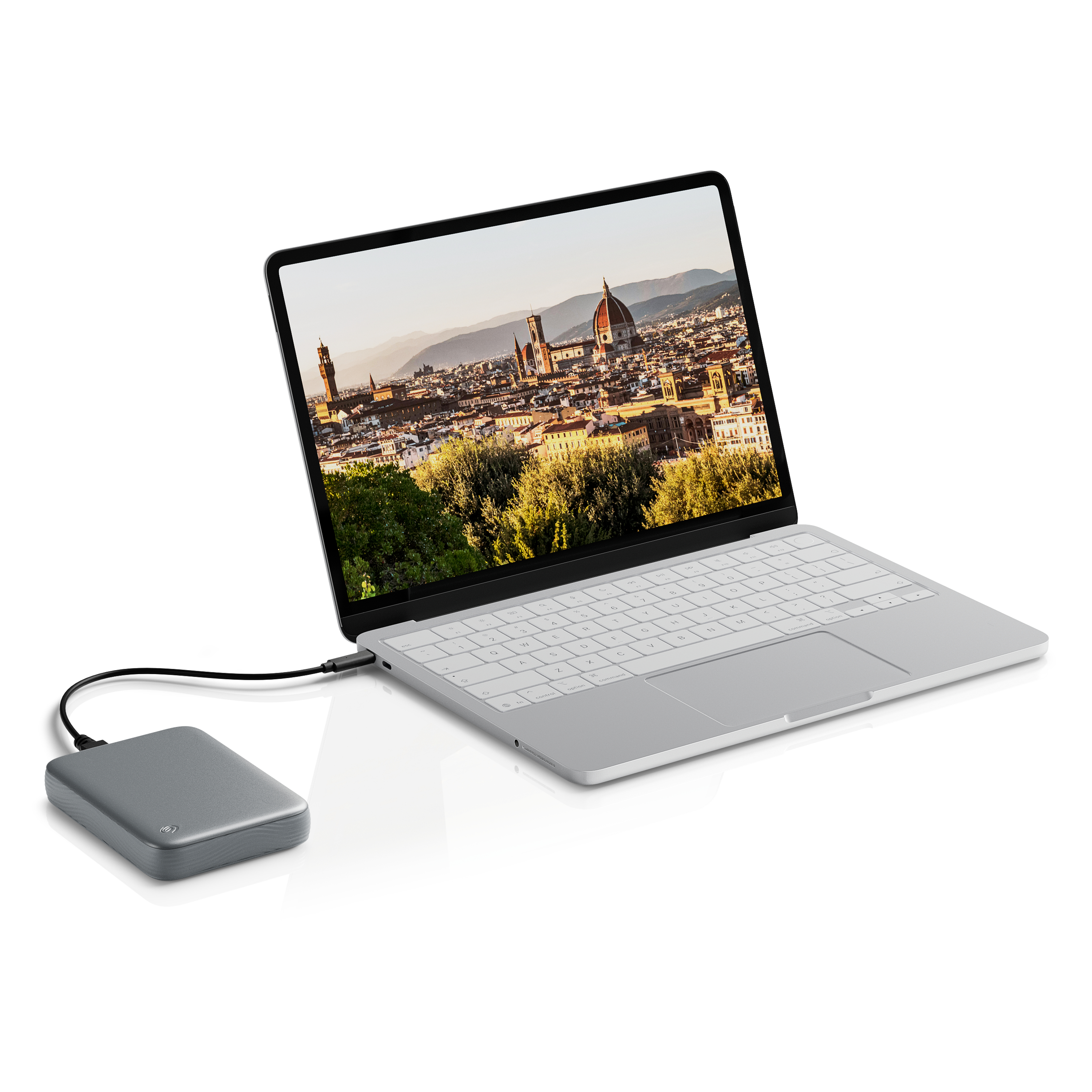 Ein silberner Laptop mit einem Stadtbild auf dem Bildschirm ist über ein Kabel mit einer externen Festplatte verbunden.