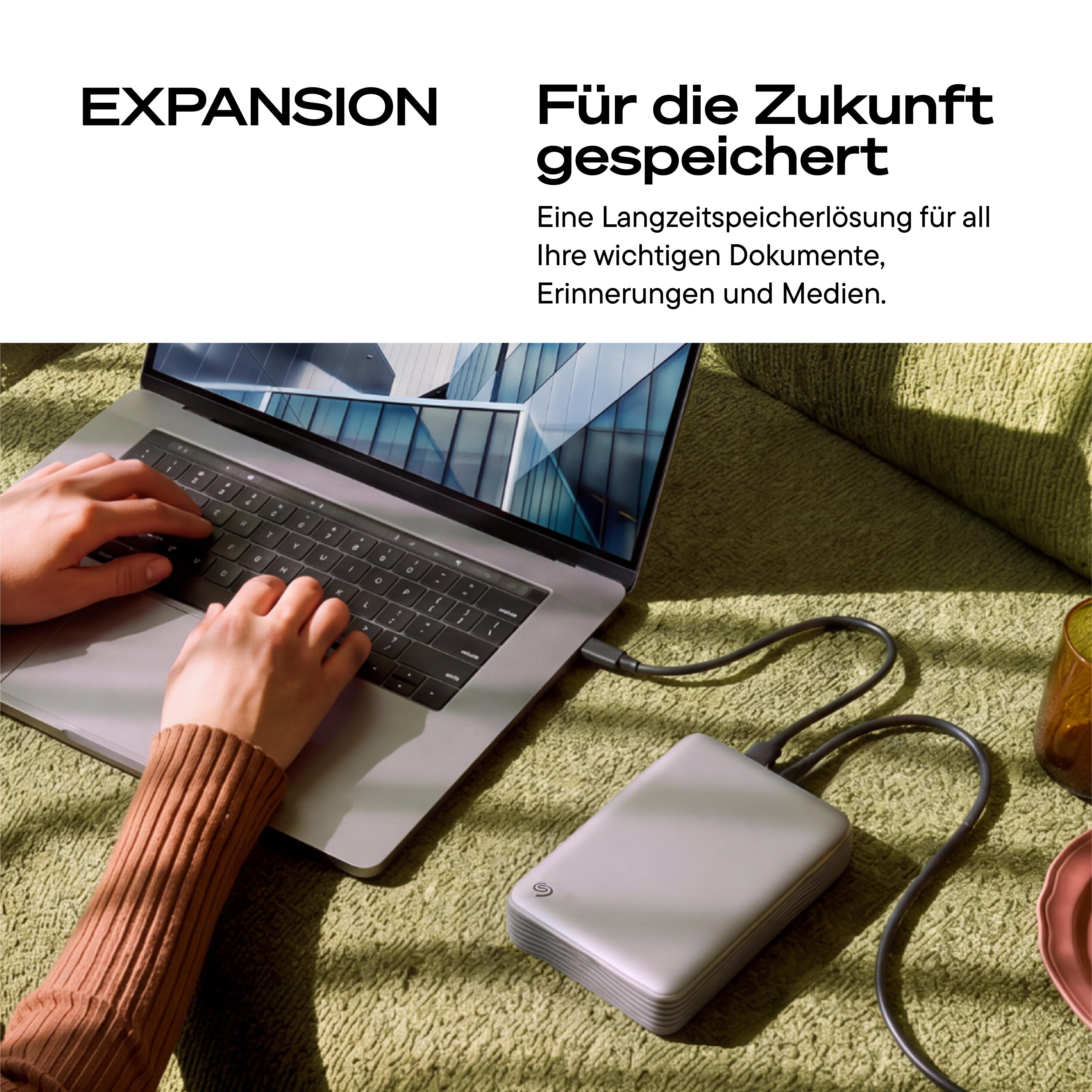 Person tippt auf Laptop, verbunden mit externer Festplatte auf grünem Sofa.